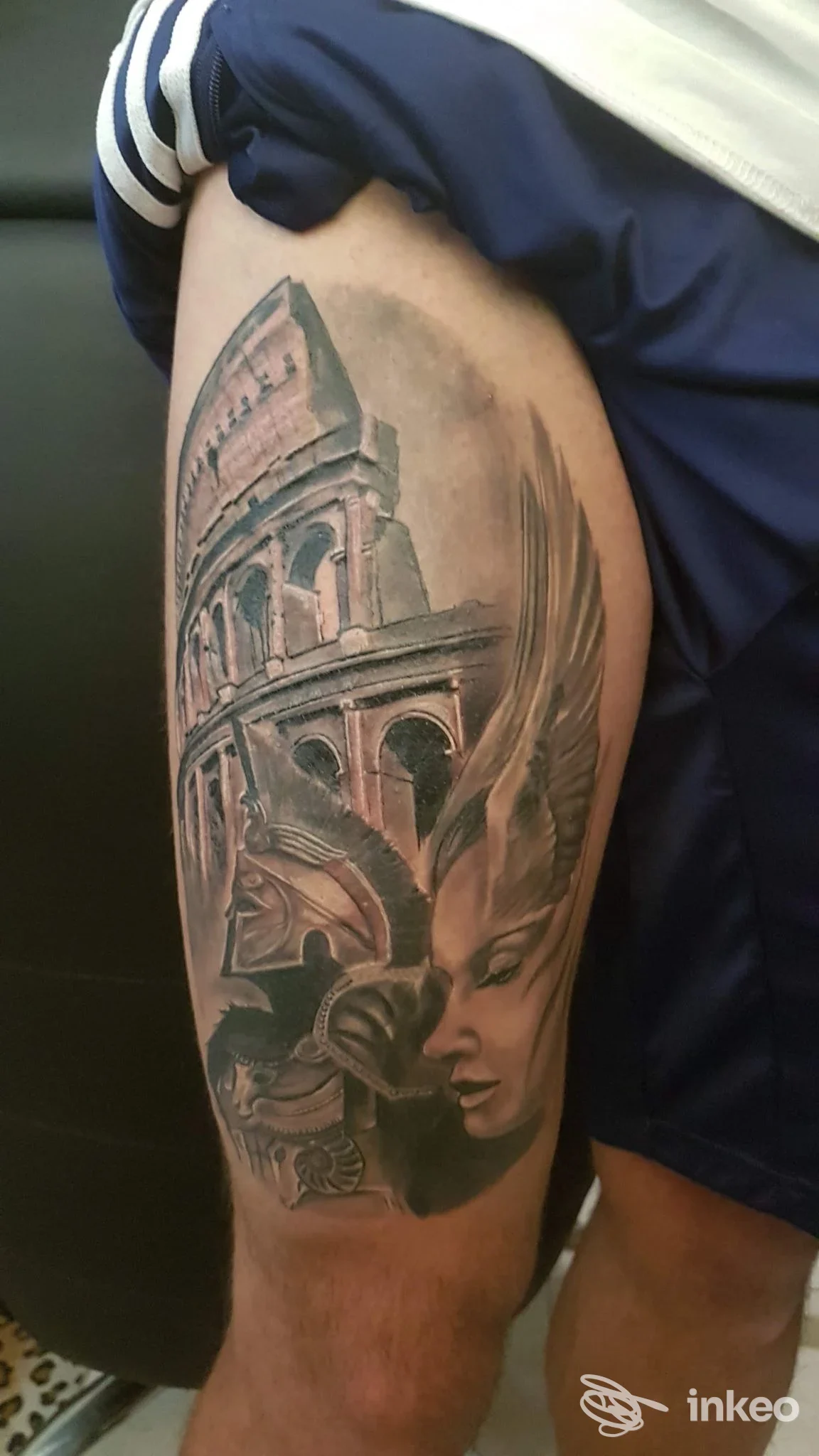 Tattoo realistico sulla gamba raffigurante l’Anfiteatro e un ritratto nel profilo, realizzato sulla pelle, visibile su gamba di una persona, colori in tonalità grigio-blu.