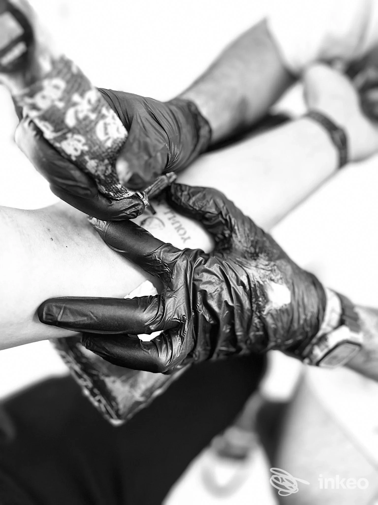 Primo piano di una sessione di tatuaggio sull'avambraccio con mani guantate e macchina in azione. REEDA TATTOO, San Severo.