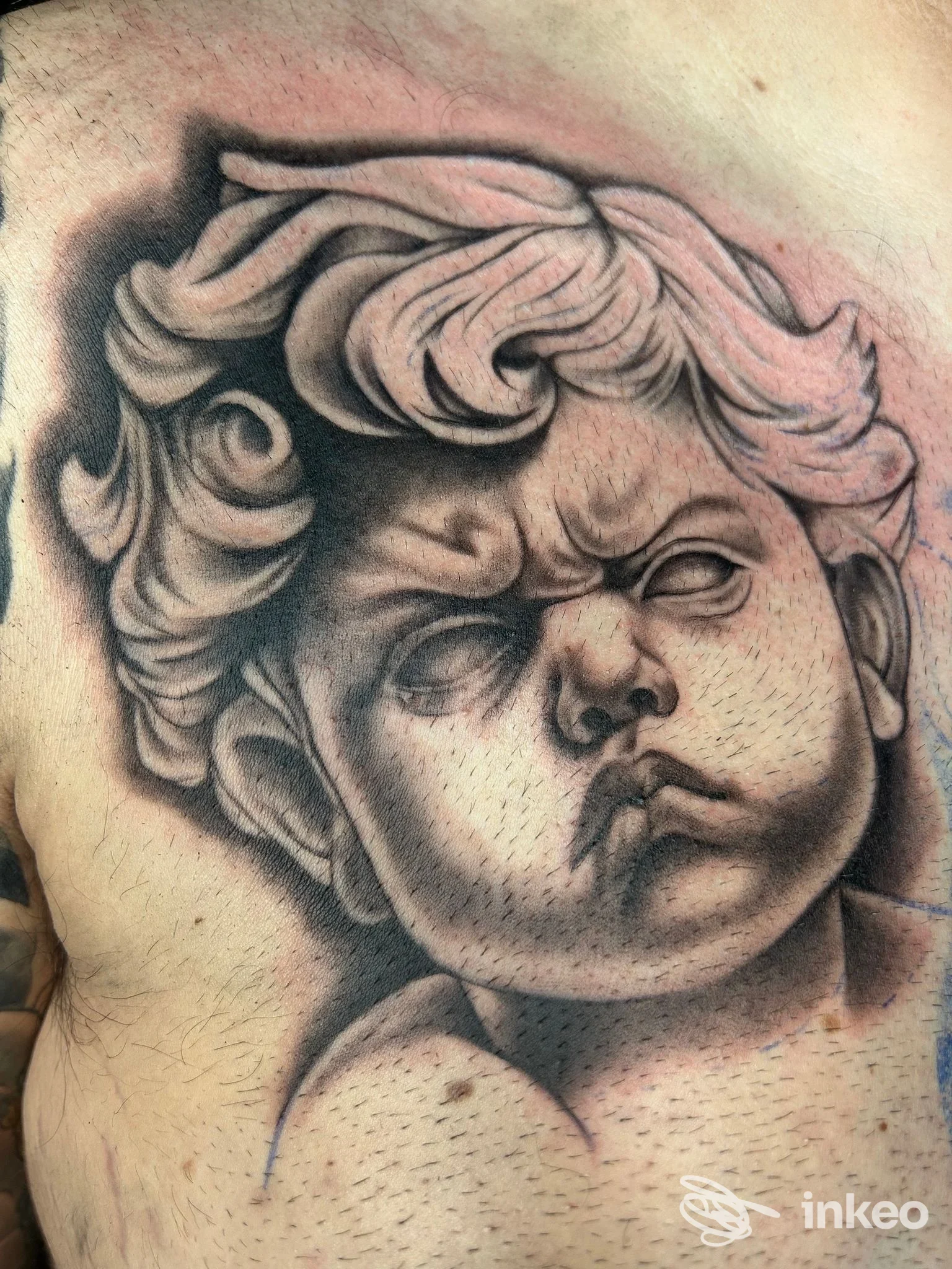Tatuaggio in bianco e nero di un putto sul petto, realizzato da REEDA TATTOO a San Severo, con dettagli ombrati e puntinati.