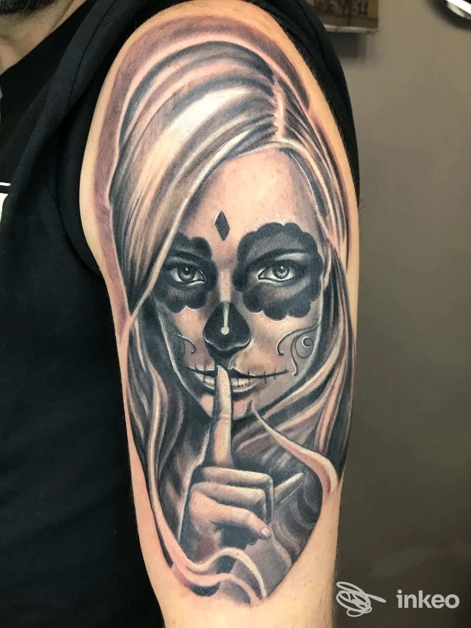 Tatuaggio realistico in bianco e nero di volto femminile calavera e gesto del silenzio sul braccio, foto da Oldskulltattoo, Erchie.