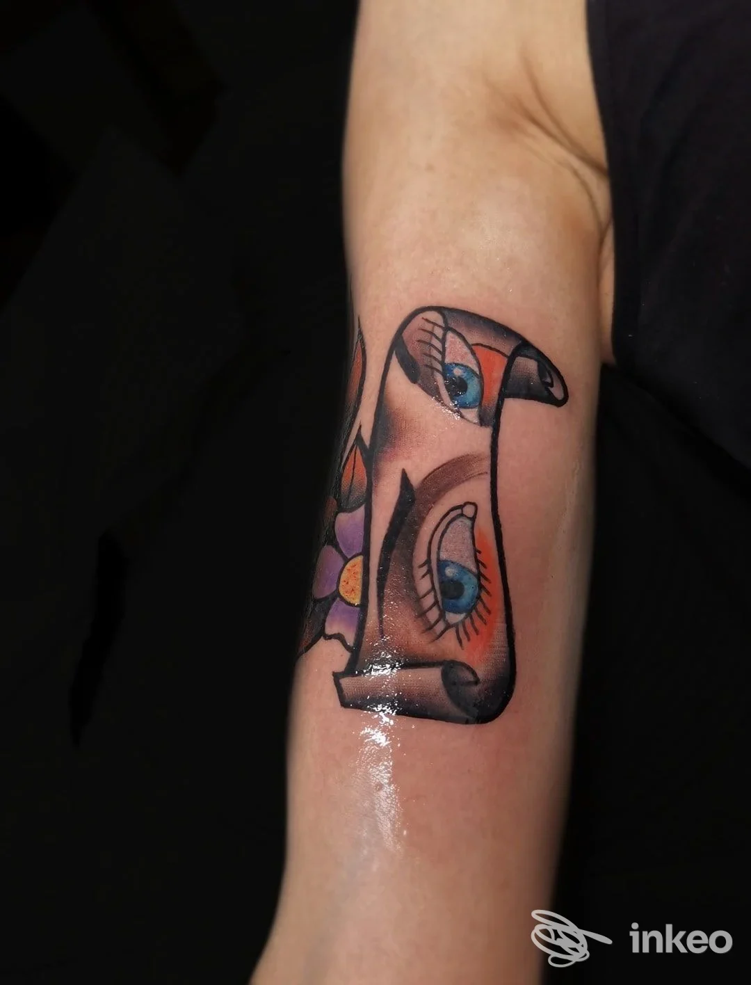 Tatuaggio su avambraccio interno: pergamena con occhi stilizzati e fiore, Scream Tattoo Ink, Altamura.