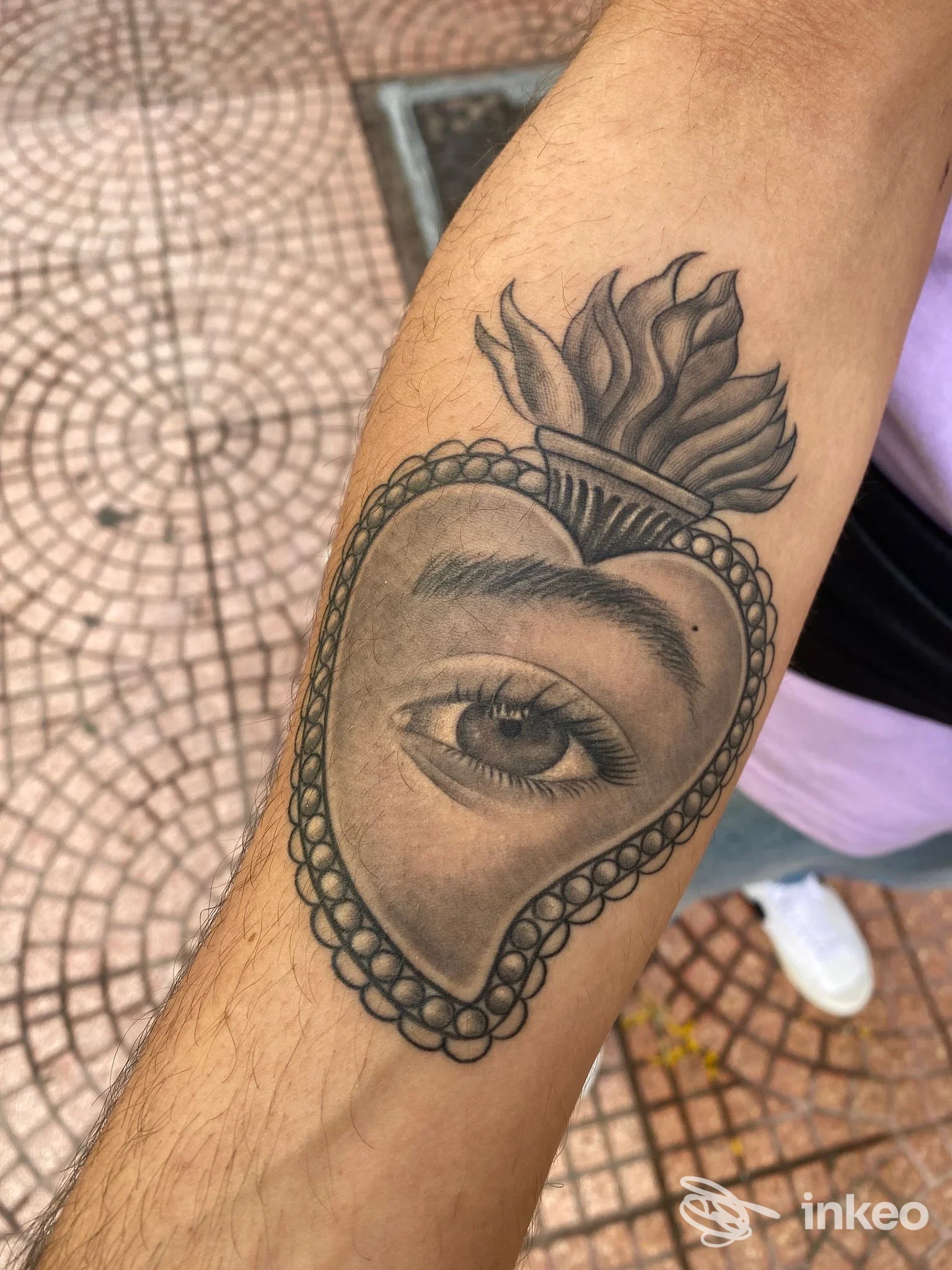 Primo piano dell'avambraccio con tatuaggio a cuore fiammeggiante che contiene un occhio realistico, foto per Tattoo Ink Peppe Valentini, Taranto.