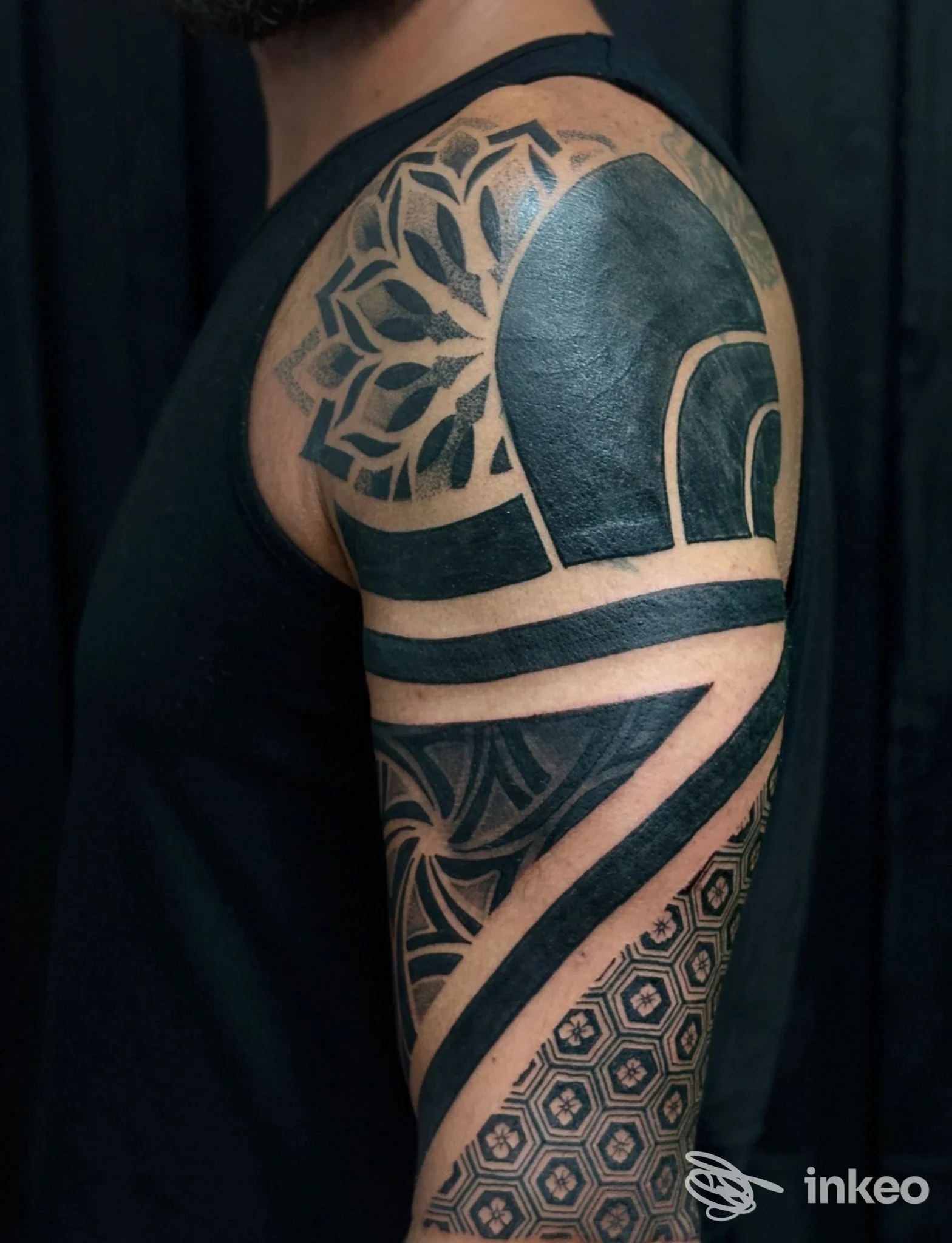 Tattoo a manica su braccio, motivo geometrico con mandala in nero su pelle reale, sfondo scuro.