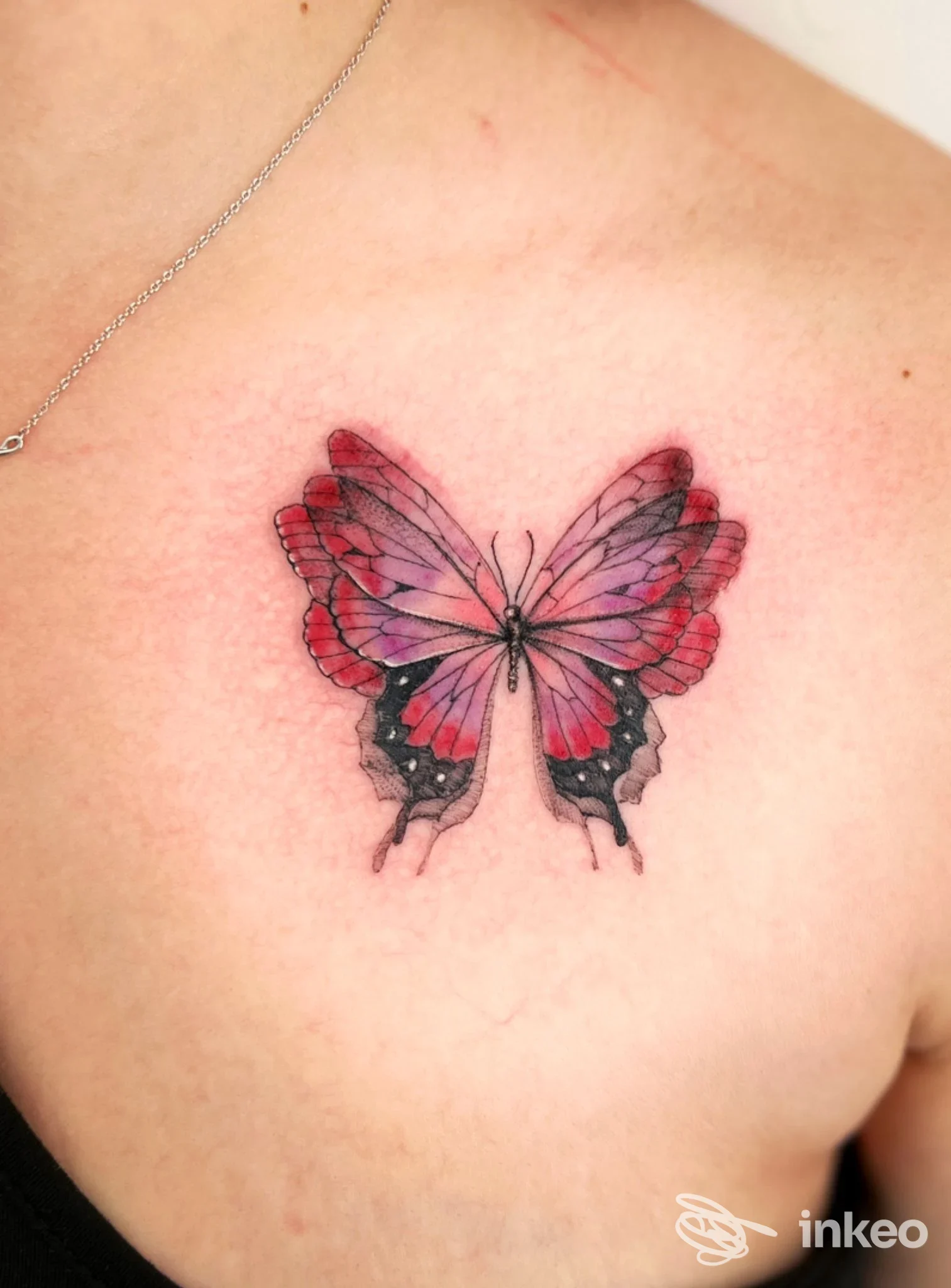 Tattoo reale di una farfalla rosa-viola su spalla/parte alta della schiena, niente volto visibile, pelle liscia, colori vividi.