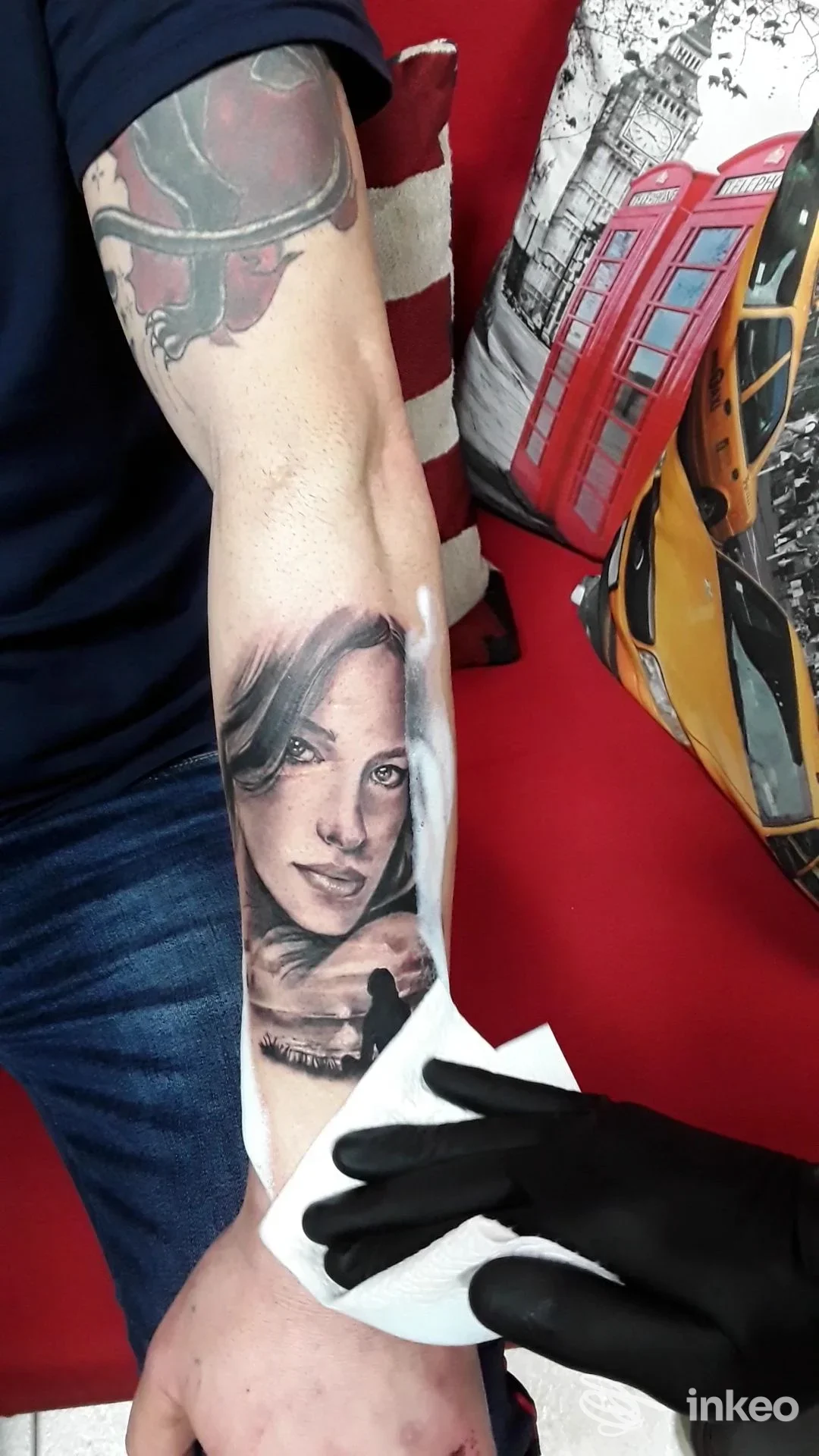 Tatuaggio ritratto realistico su avambraccio, immagine dallo Studio Tatuaggi Di Loche Gian Marco a Uta, operatore con guanto nero pulisce l'area.