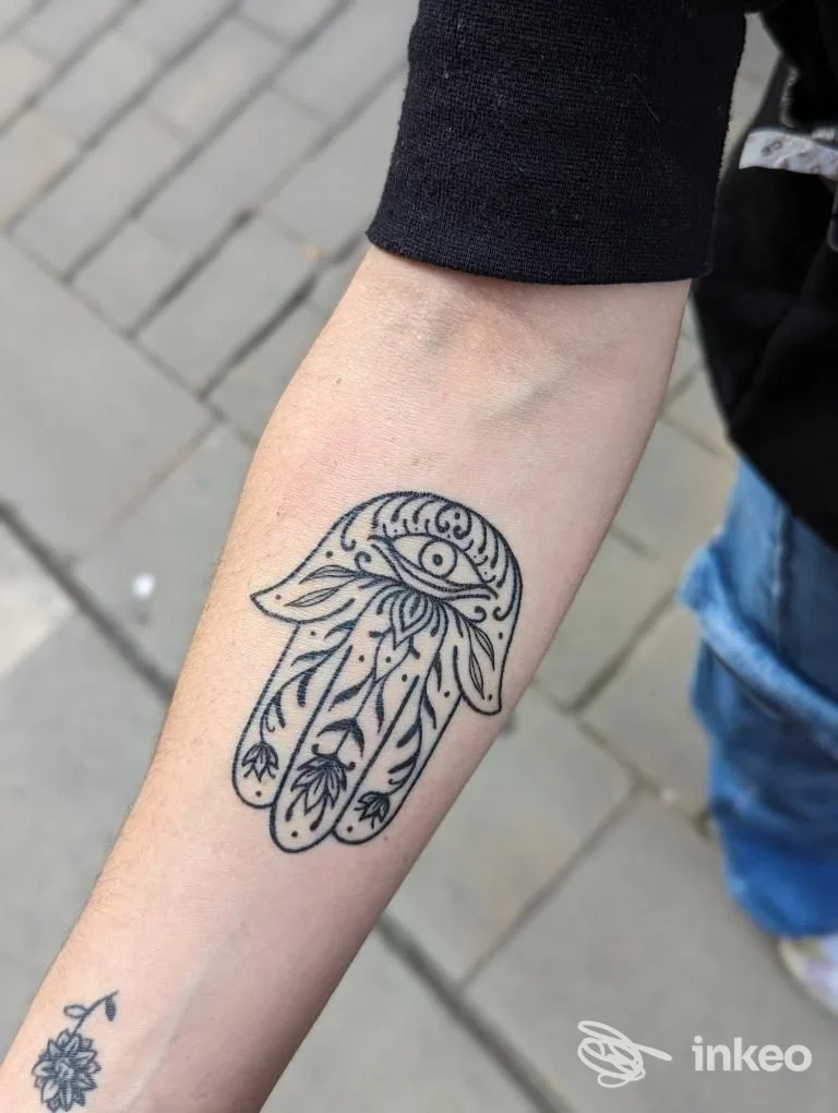 Tatuaggio Hamsa in linea nera sull'avambraccio con dettagli ornamentali, fotografia di Tattoo house a Cala Caterina.