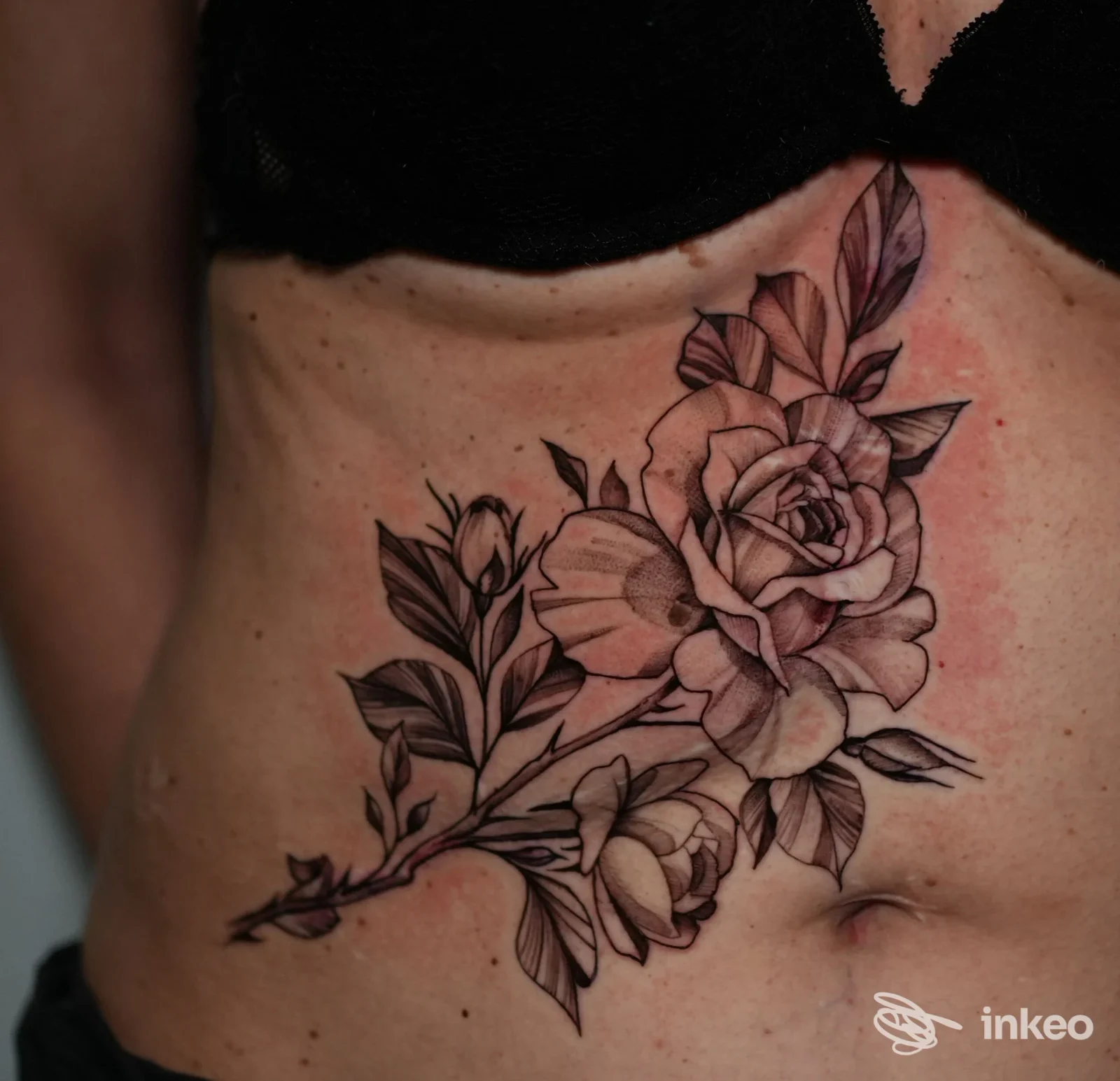 Tatuaggio floreale nero e grigio sull'addome eseguito da Stigma Tattoo a Porto Torres, dettaglio del fiore e delle foglie.