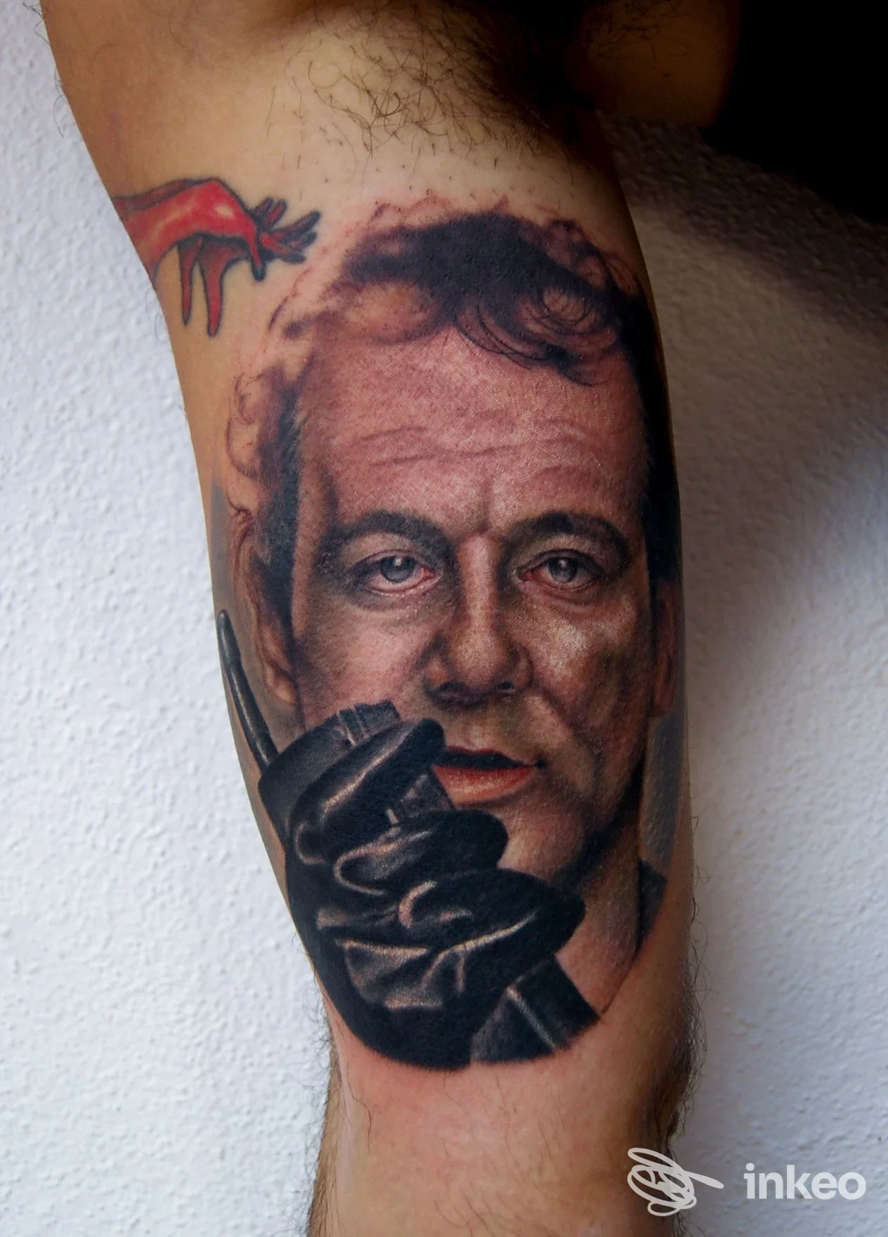 Ritratto fotorealistico tatuato sull'avambraccio con mano guantata nera e dettaglio rosso, lavoro di T'ink tattoo studio ad Alghero.