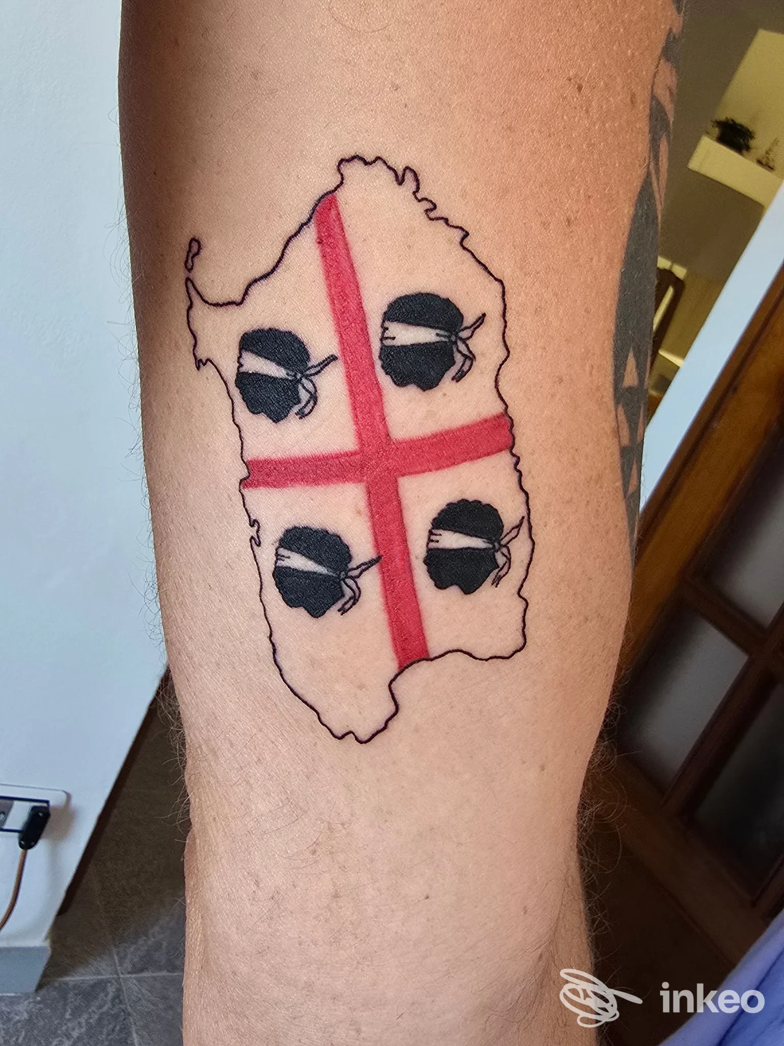 Tatuaggio su avambraccio con sagoma d'isola, croce rossa e quattro teste bendate, foto fornita da Three Little Monkeys Tattoo Studio, Sassari.