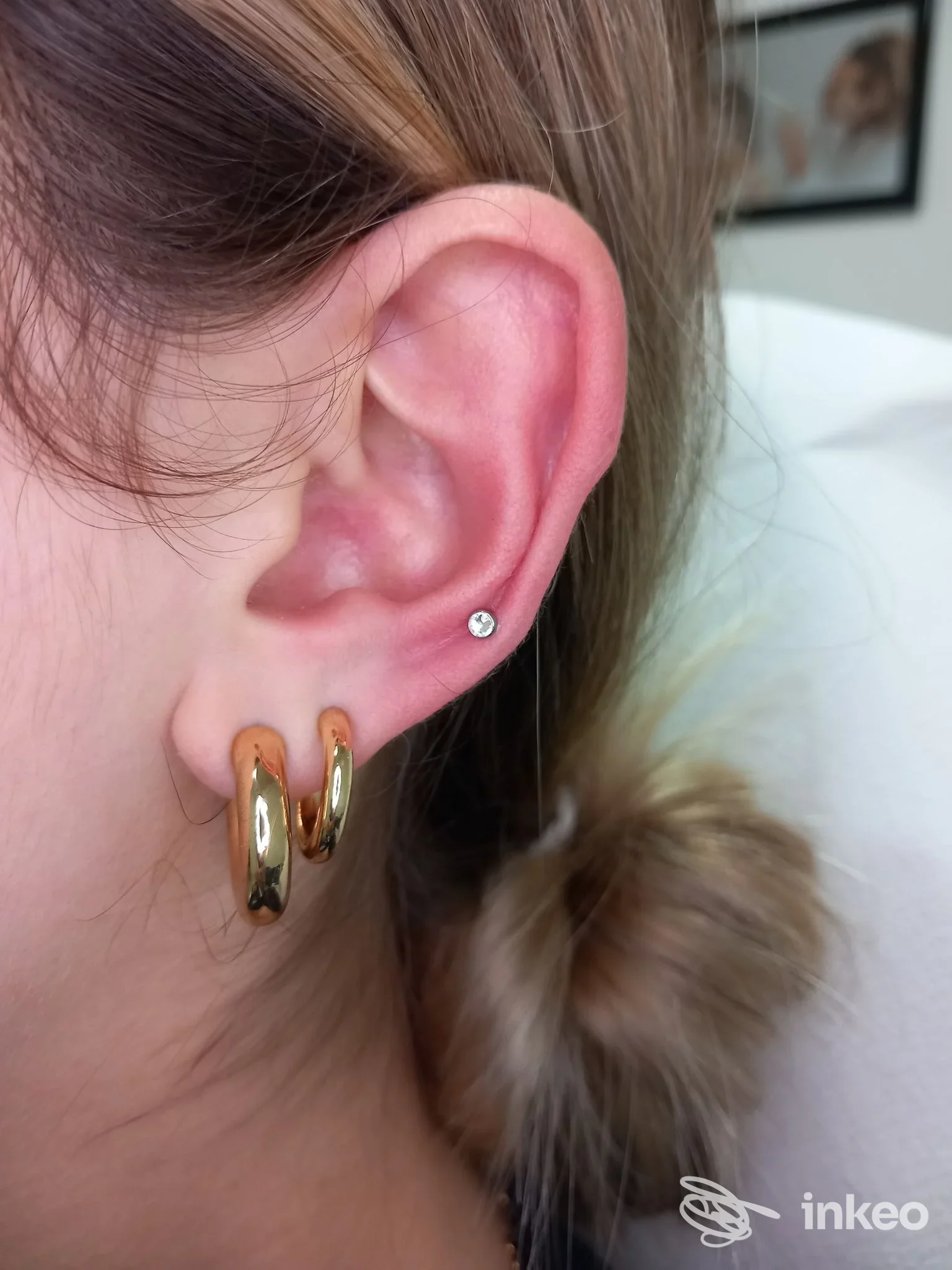 Primo piano di un orecchio con due cerchi dorati e un micro piercing, fotografia per Truccatore-Piercing, Olmedo.