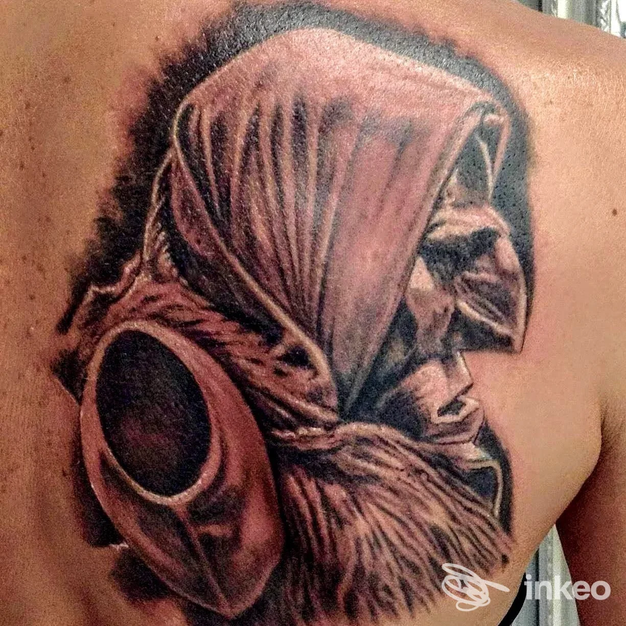 Tatuaggio realistico in black & grey di un volto incappucciato sulla parte alta della schiena, realizzato da axis tatuaggi e body piercing, Sestu.