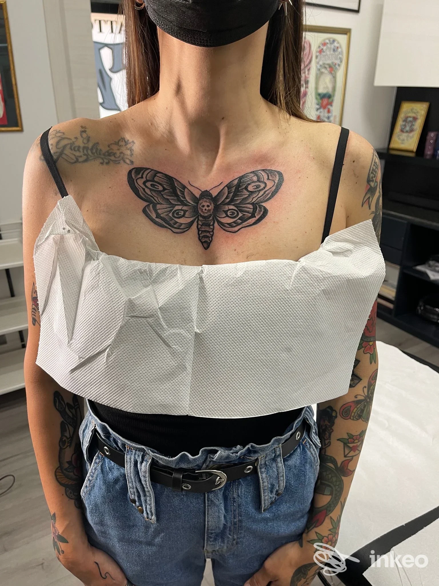 Donna con mascherina mostra un grande tatuaggio a forma di falena sul petto, foto da 379 tattoo studio a Cagliari.