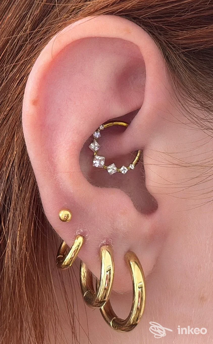 Primo piano di un orecchio con più piercing in oro e un anello con zirconi, Alessandro Daga Piercing, Cagliari.