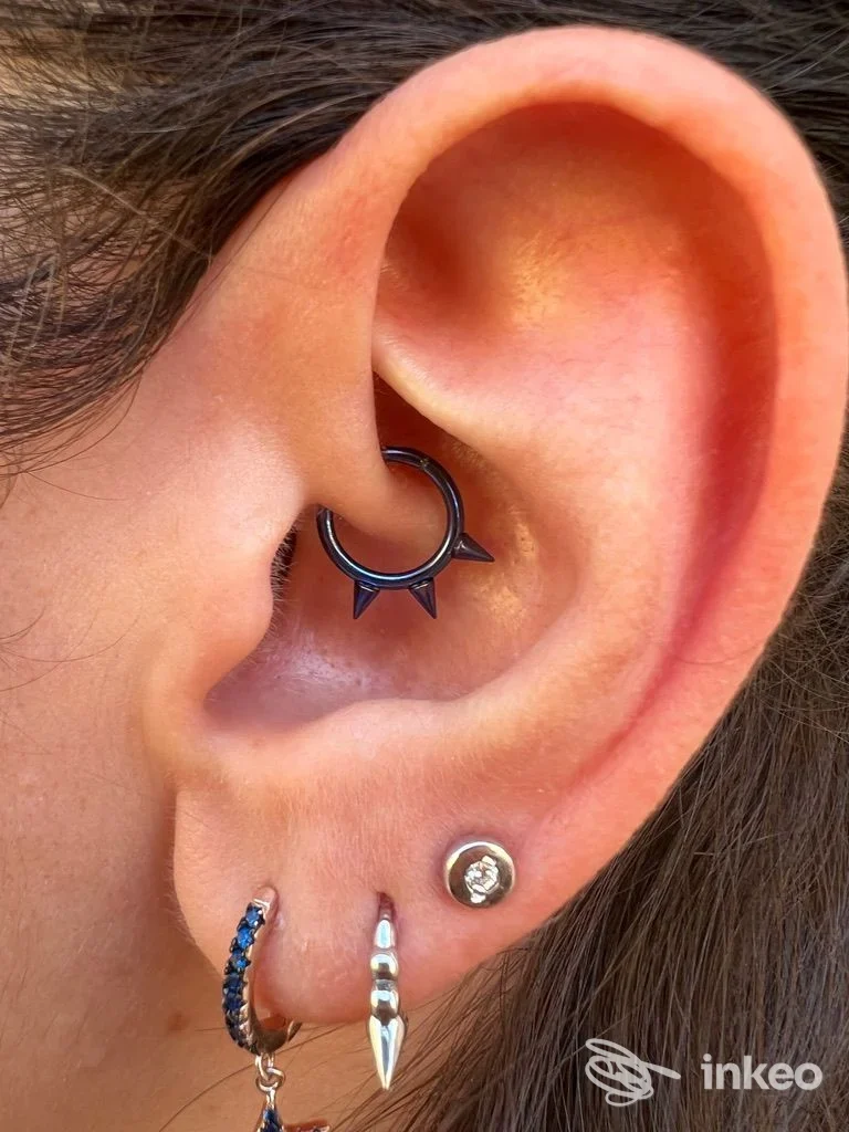 Orecchio con più piercing visibili, incluso anello nero decorato nella parte interna e gioielli ai lobi — Alessandro Daga Piercing, Cagliari.