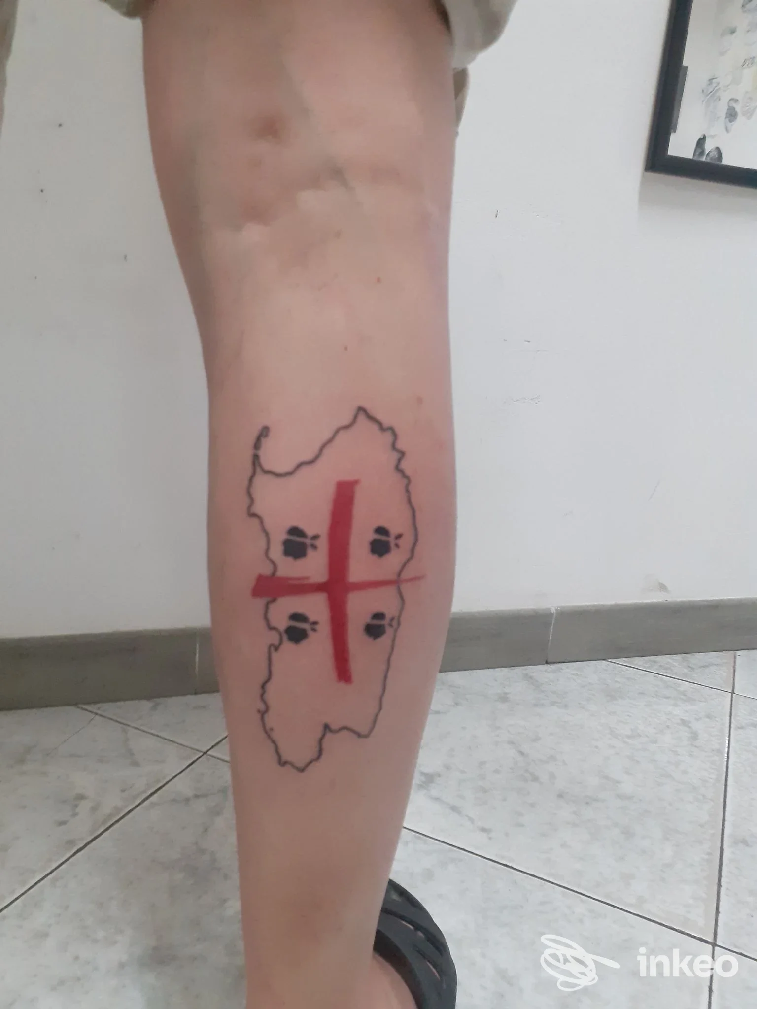 Tatuaggio sul polpaccio con contorno della Sardegna, croce rossa e quattro simboli neri, scattato presso Battle Tattoo a Cagliari.