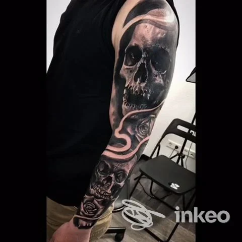 Manica tatuata con teschi e rose al Black Apple Tattoo Studio, La Caletta, su braccio sinistro di una persona.