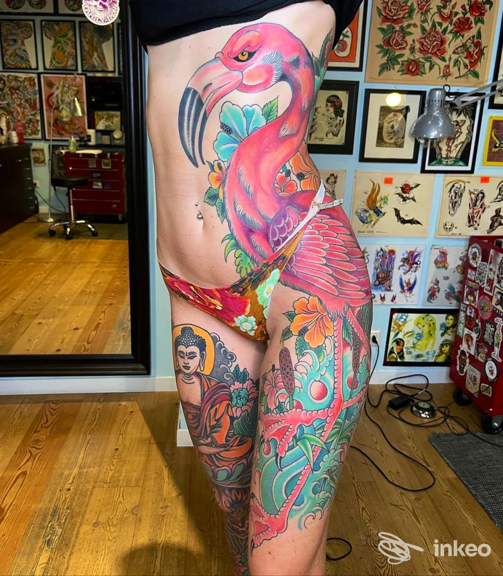 Tatuaggio colorato di un fenicottero rosa con fiori, esteso sul busto e sulla coscia sinistra di una persona, nello studio The Black Pearl Tattoo Parlour.