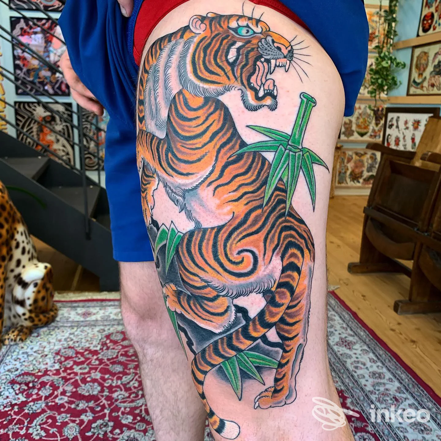 Tattoo visibile sulla coscia esterna: tigre arancione con strisce nere e elementi verdi simili a bamboo, realizzato sulla pelle di una persona.