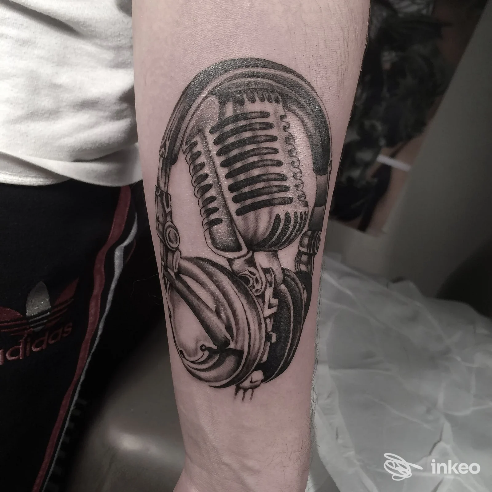 Tatuaggio sul braccio raffigurante un microfono vintage con cuffie, realizzato sulla pelle.