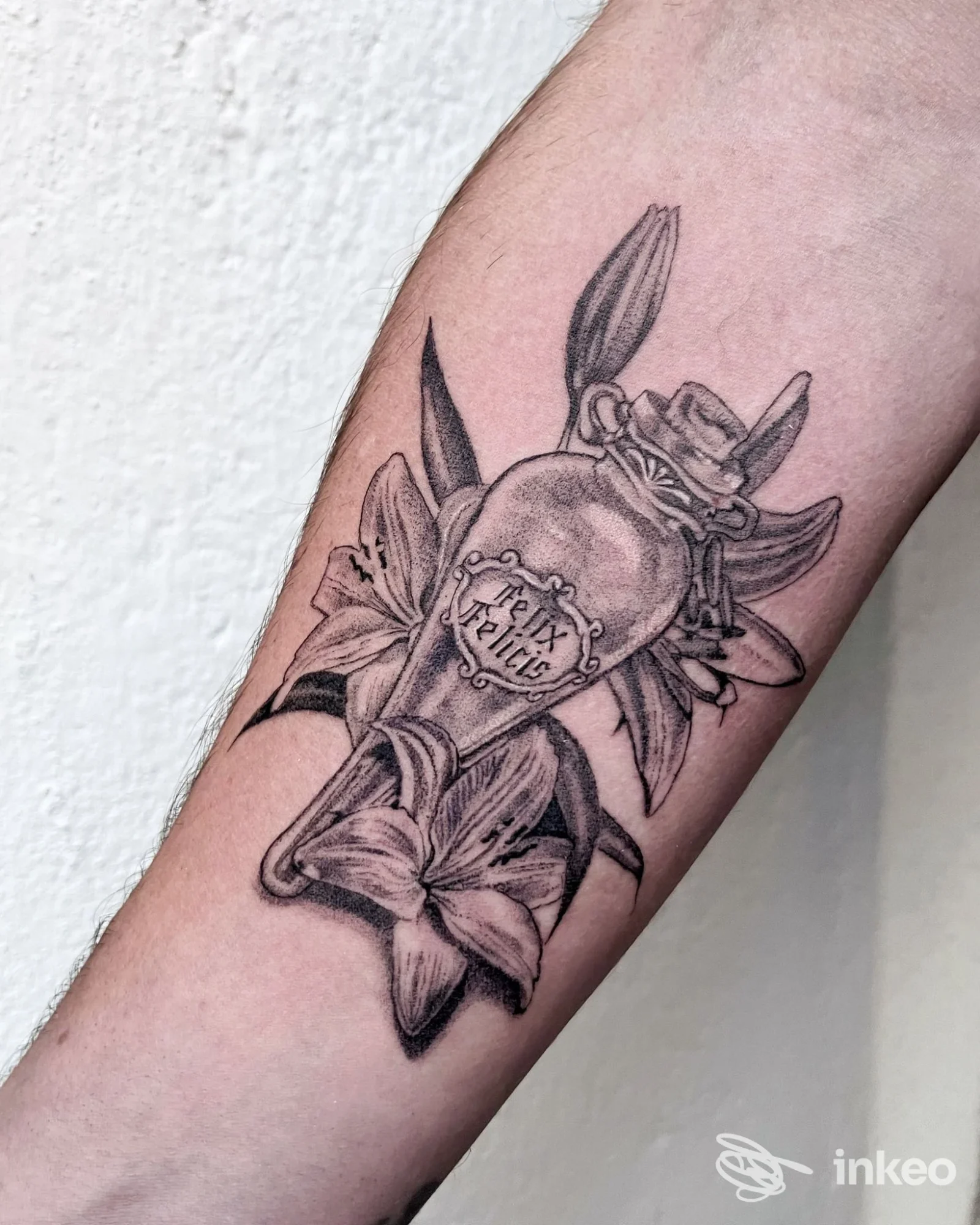 Tatuaggio in bianco e nero con bottiglia e fiori sull'avambraccio, realizzato da Atelier Piercing & Tattoos a Cagliari.