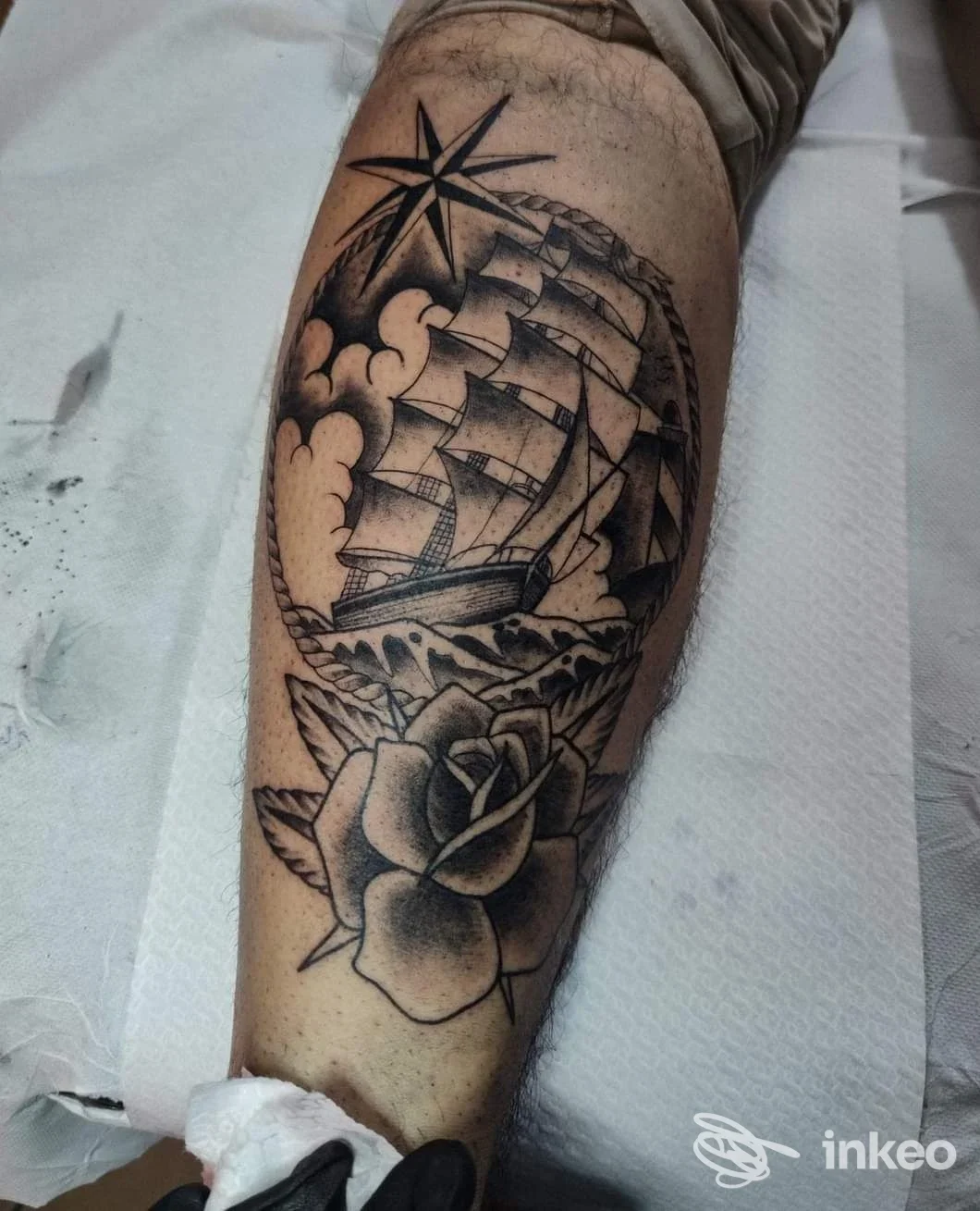 Tatuaggio in nero e grigio su polpaccio con nave a vele, rosa e stella nautica, Corazón Espinado Tattoo Shop, Orosei.