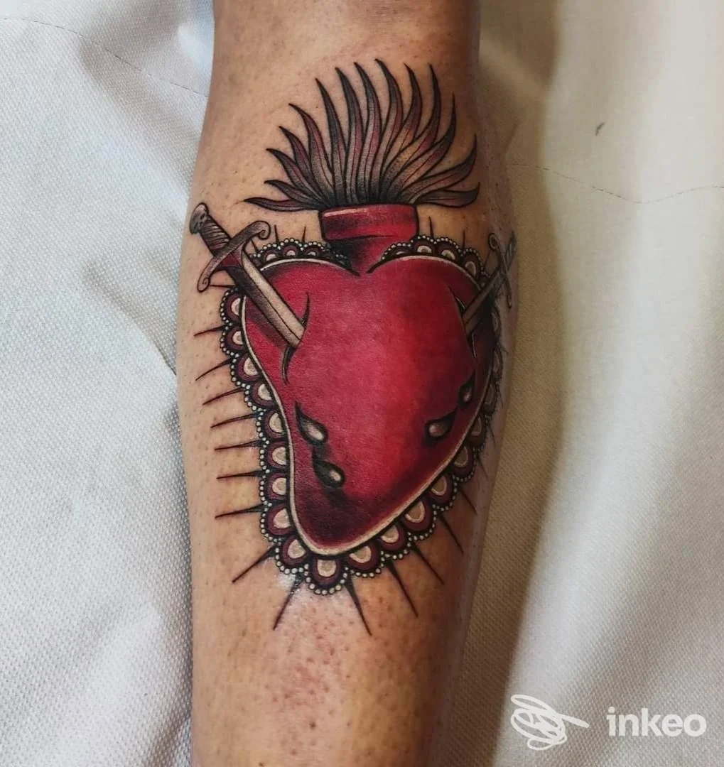 Tatuaggio a colori raffigurante un cuore sacro trafitto da lame sull'avambraccio; immagine fornita da Corazón Espinado Tattoo Shop, Orosei.