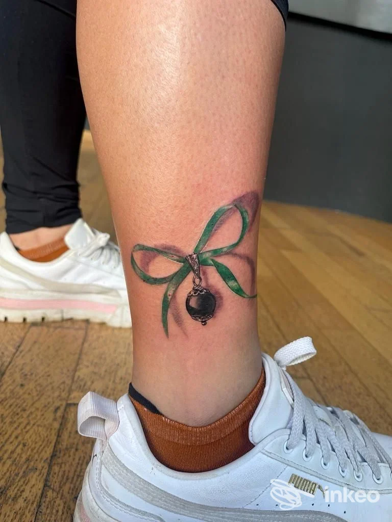 Tatuaggio a fiocco verde con ciondolo sul polpaccio, eseguito da Crazy Cat Tattoo a Cagliari.
