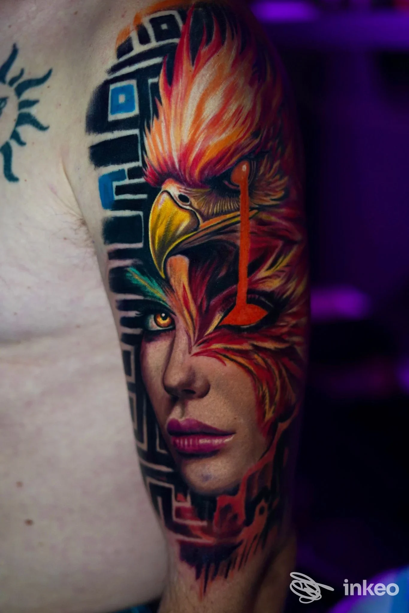 Tatuaggio a colori su braccio con volto fotorrealistico e piume arancioni, foto fornita da DaVinci tattoo Studio, Assemini.