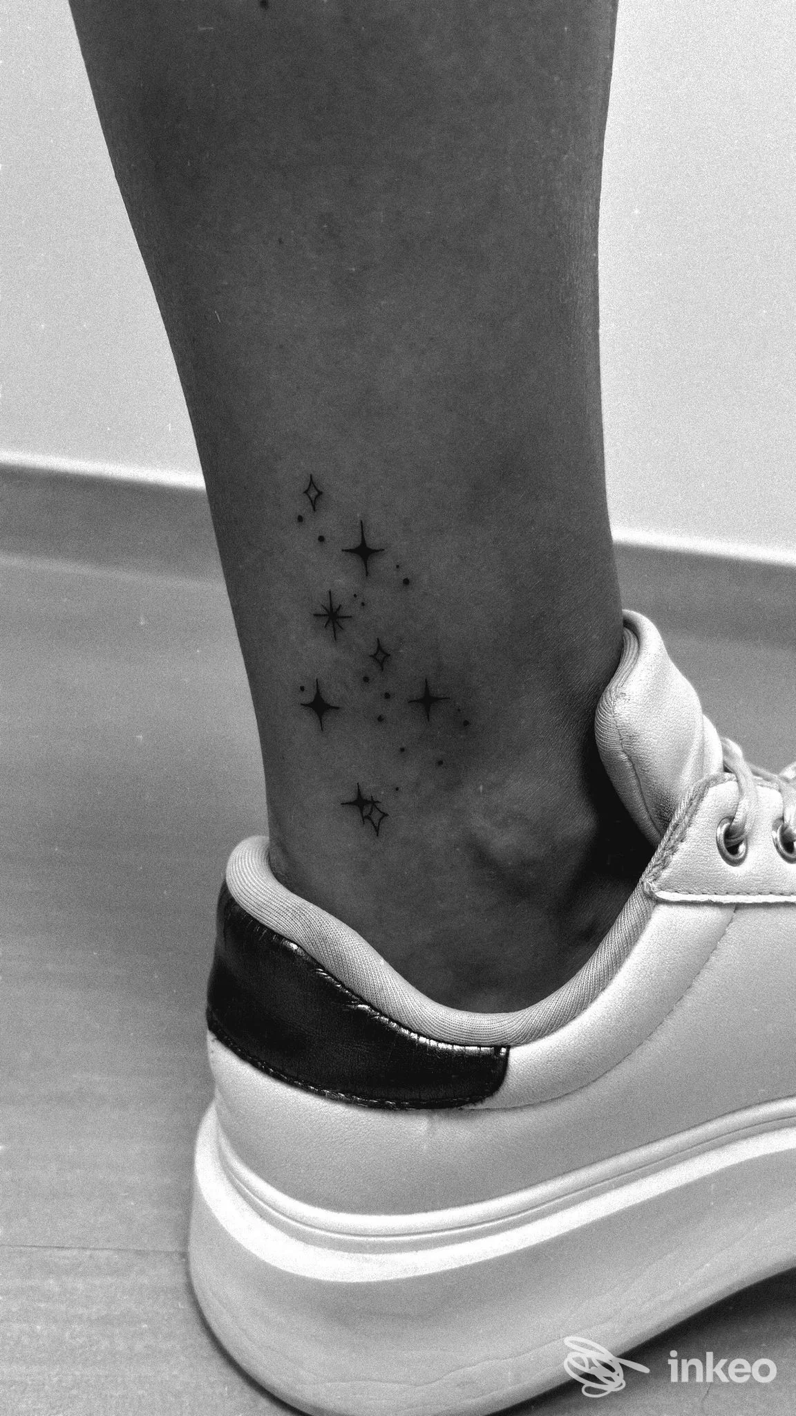 Tatuaggio minimal di piccole stelline sul lato della caviglia, foto in bianco e nero. EleTattoo, Lanusei.