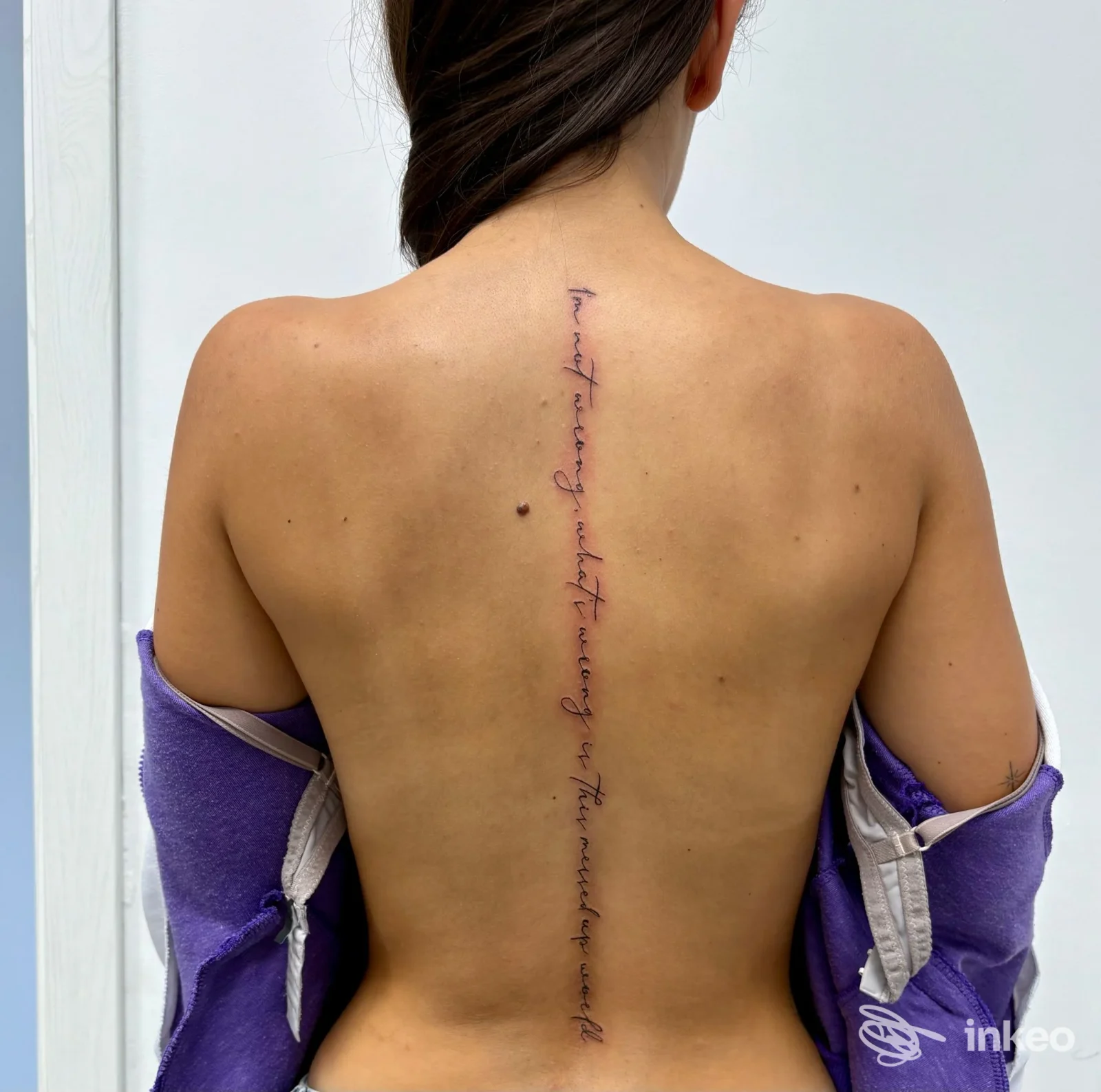 Fotografia di un tatuaggio testuale verticale lungo la colonna vertebrale su schiena femminile, realizzato da EleTattoo a Lanusei, vista posteriore.