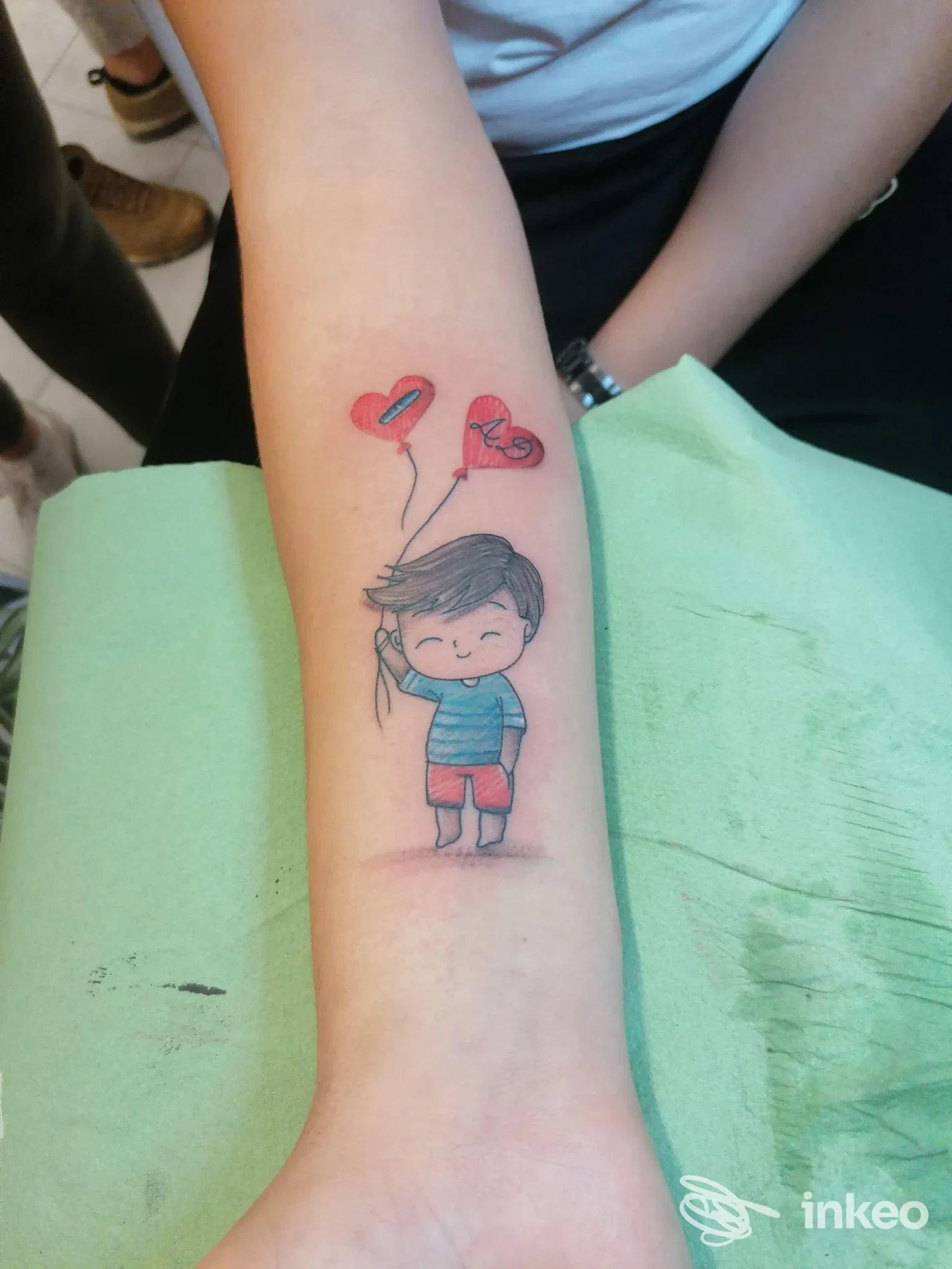 Tatuaggio sull'avambraccio di un bimbo in stile cartoon con due palloncini a forma di cuore, foto dallo studio Eternity 17 Tattoo Shop, Selargius.
