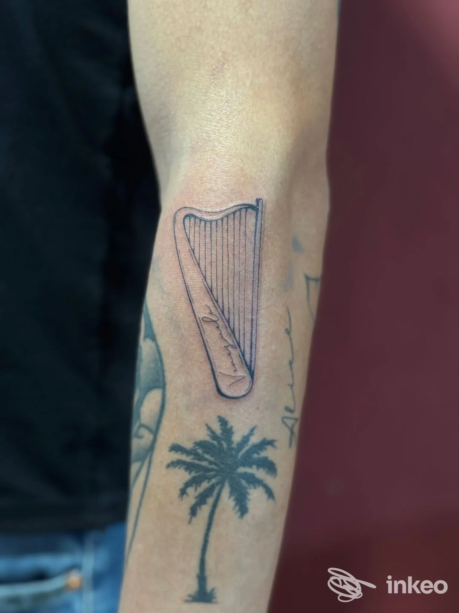 Tatuaggi in bianco e nero su avambraccio: arpa stilizzata sopra palma. Foto per Forgia Custom Tattoo, Alghero.