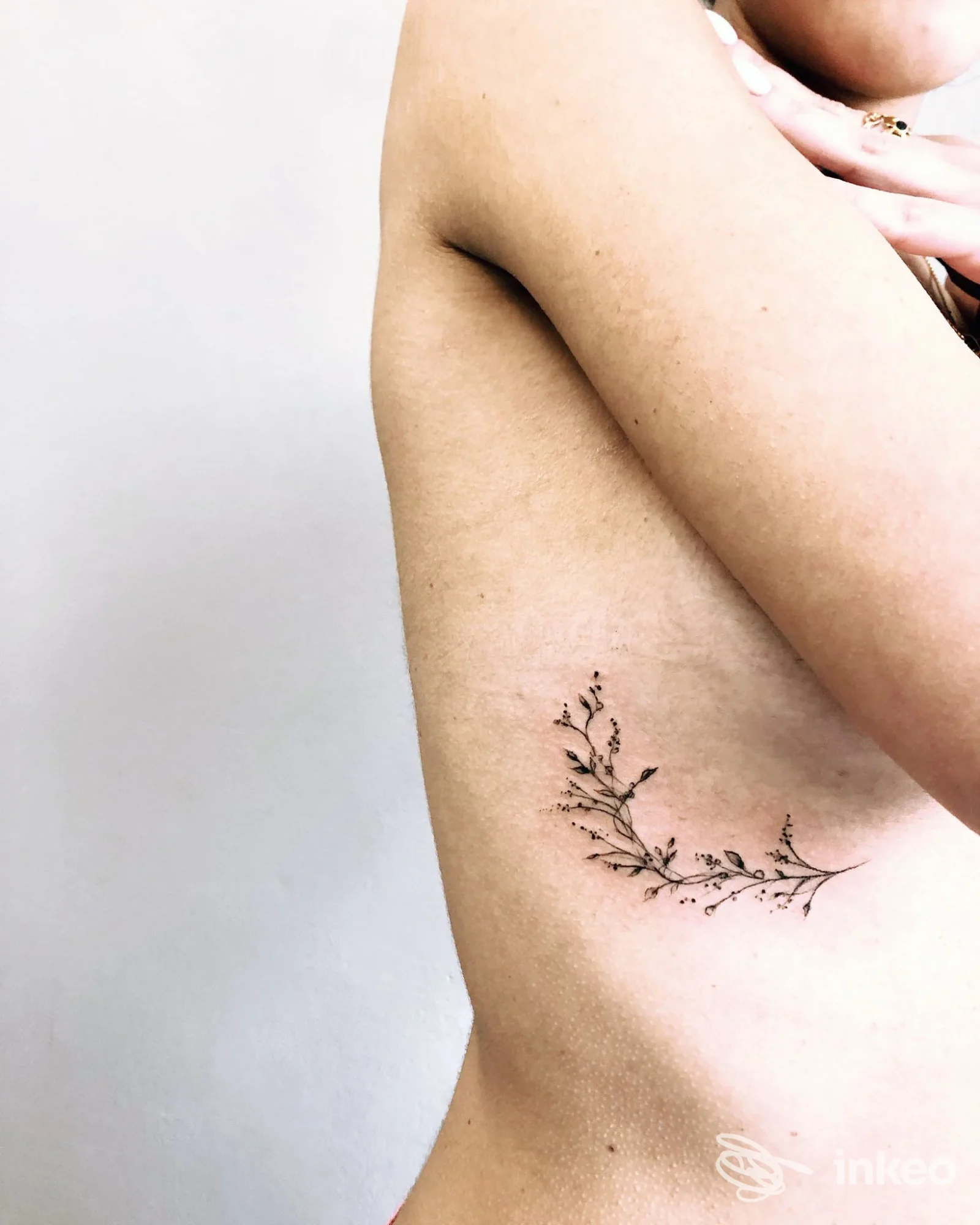 Tattoo di un ramo di foglie inciso sulla pelle del fianco, visibile a lato, senza volto umano nella foto.
