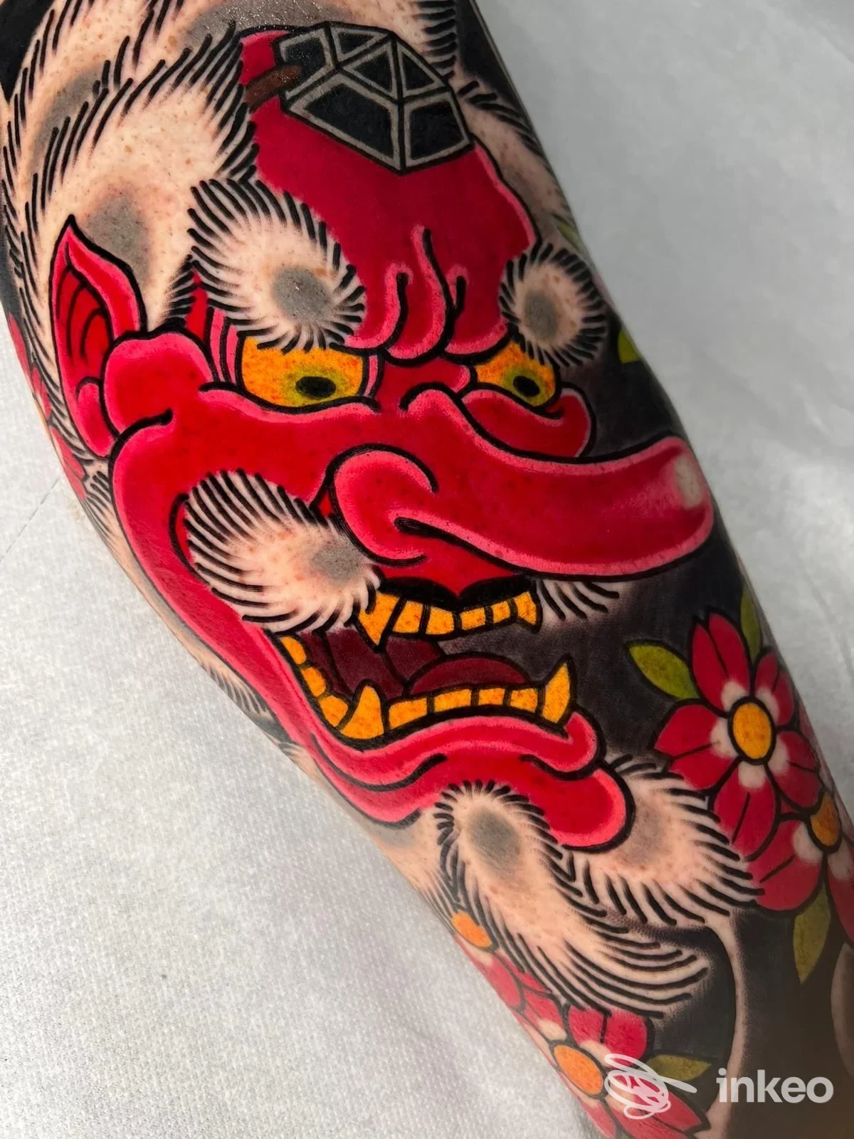 Tatuaggio a colori su avambraccio: maschera Hannya rossa con fiori, realizzato da Cagliari Classic Tattoo a Cagliari.