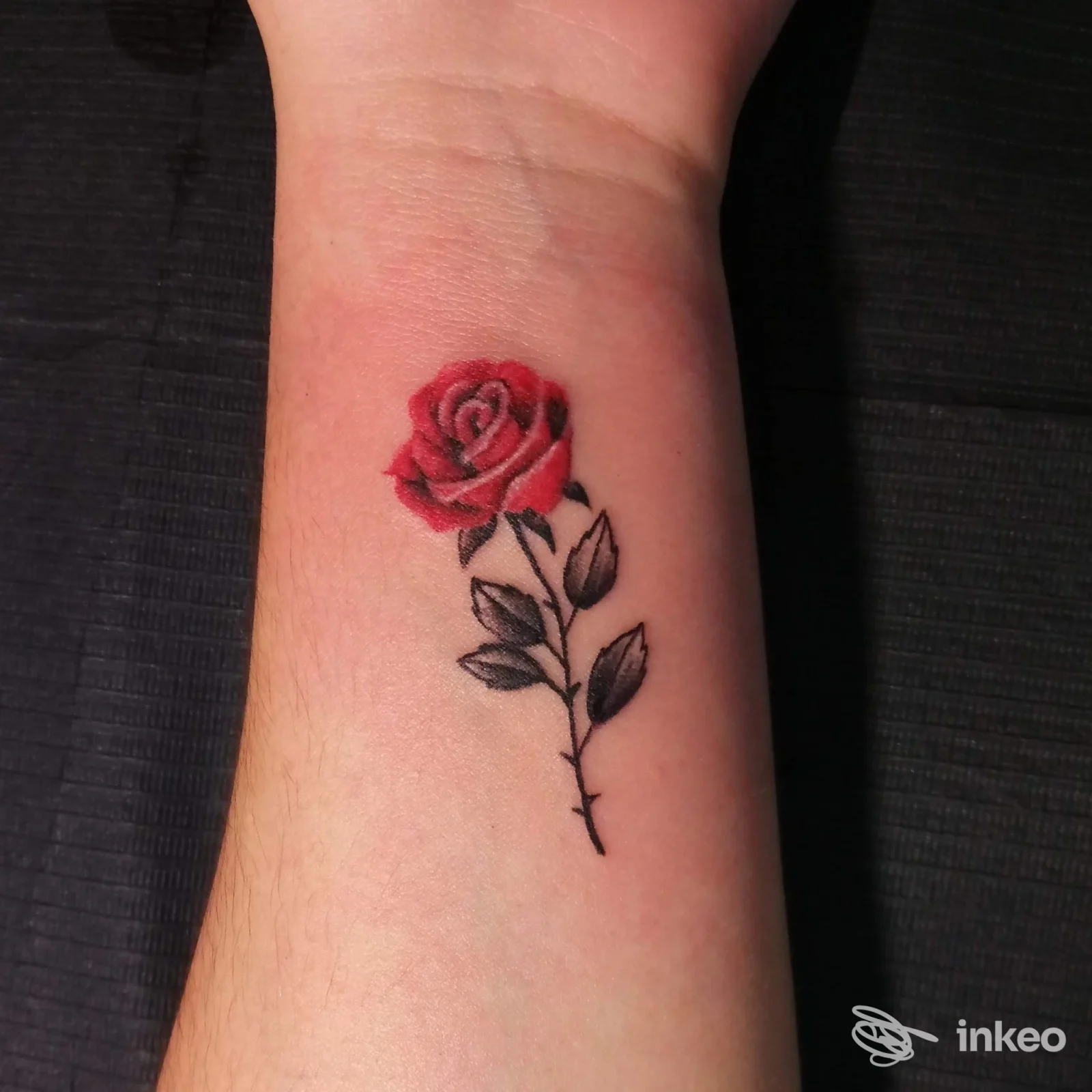 Piccolo tatuaggio di una rosa rossa sul polso, fotografato su pelle reale; immagine fornita da Gemma Body Art Tattoo di Pili Manuel, Assemini.