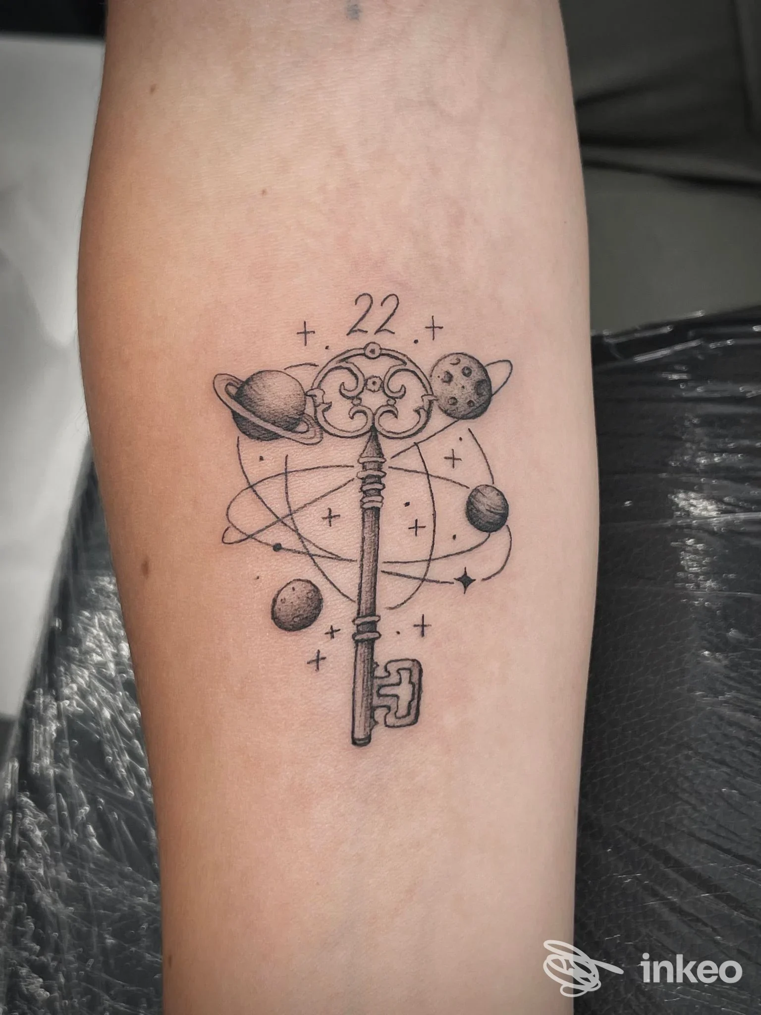 Tatuaggio in nero su avambraccio con chiave decorativa e pianeti, realizzato da INKIOSTRO studio tatuaggi a Cagliari.