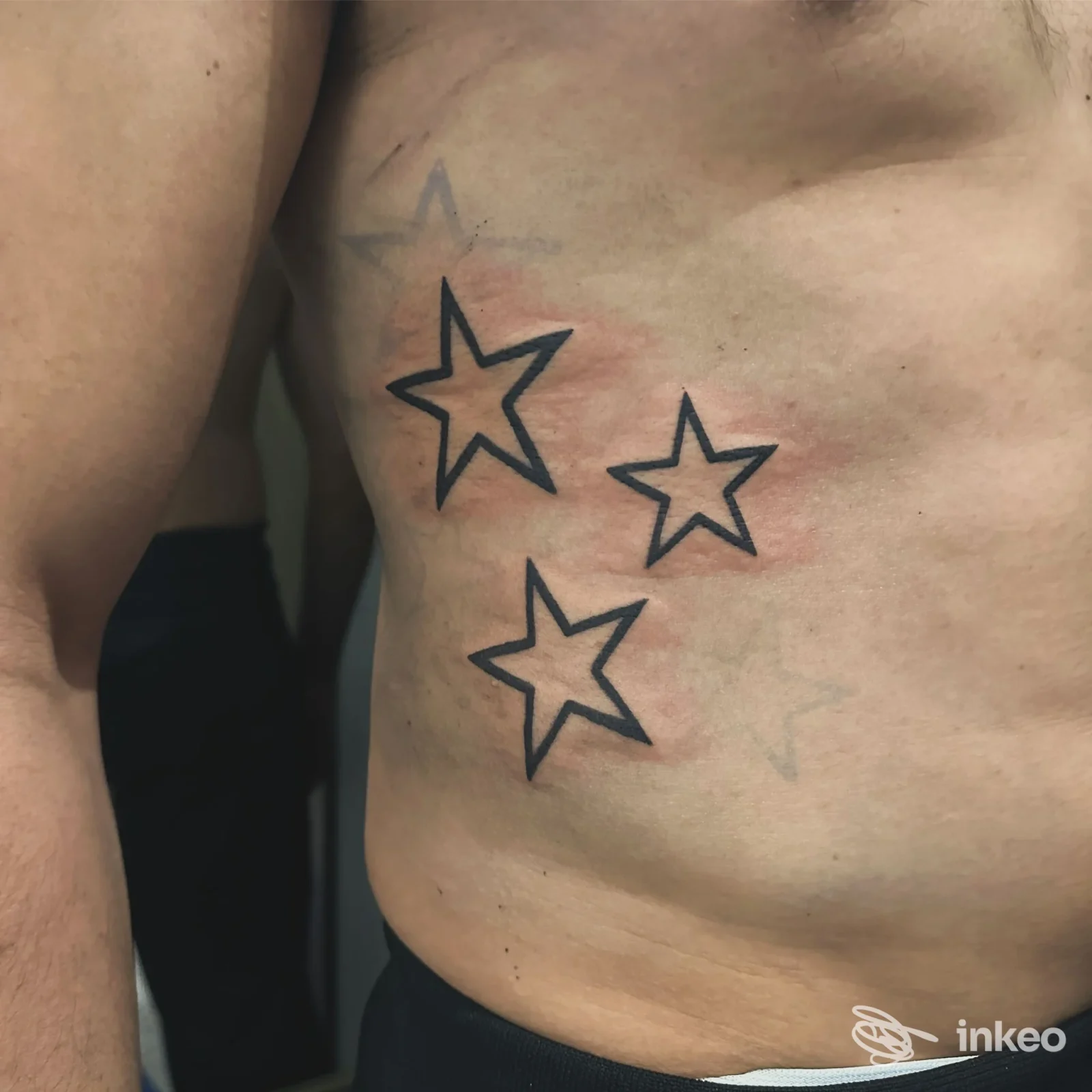 Tre stelle contornate tatuate sul fianco di un torace maschile, lavoro mostrato da KHRIS TATTOO a Pattada.
