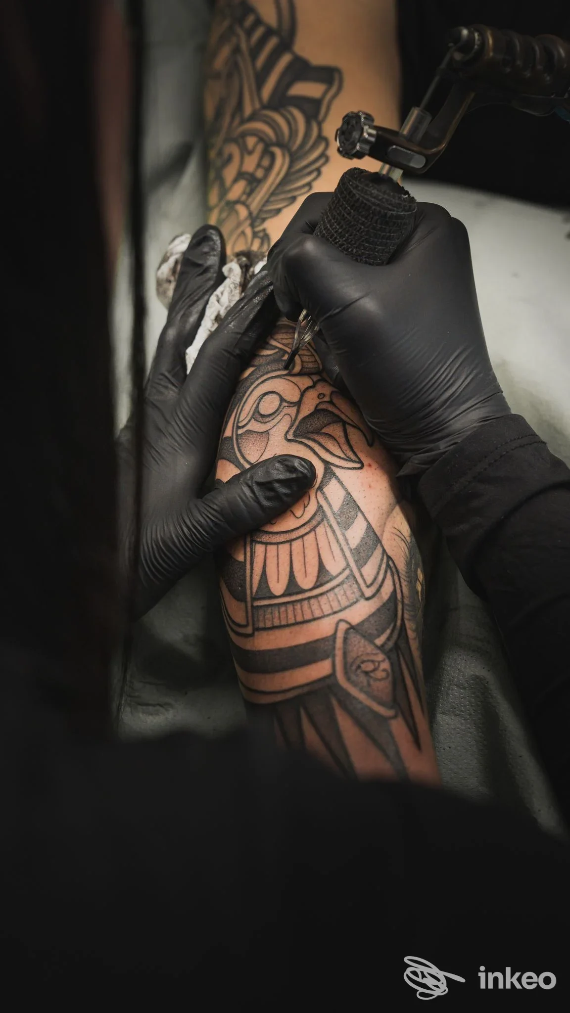 Primo piano dell'avambraccio di una persona in studio mentre un tatuatore con guanti esegue un tatuaggio; macchina e dettagli di lavoro visibili. NUMB Tattoo Parlour, Porto Torres.