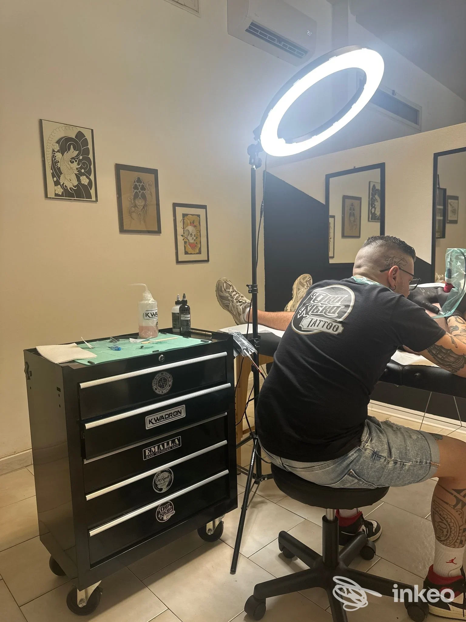Tatuatore di Oro Nero Tattoo al lavoro su un cliente nel loro studio a Quartu Sant'Elena, lampada ad anello e carrello strumenti visibili.