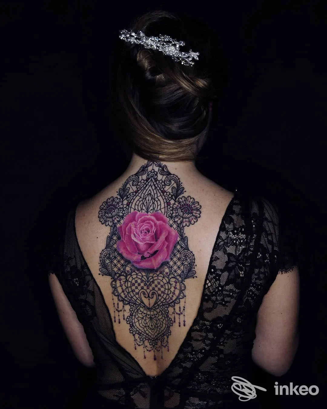 Grande tatuaggio ornamentale con rosa centrale sulla schiena; foto realizzata per Scorpiontattoo a Sassari, sfondo scuro e capelli raccolti.
