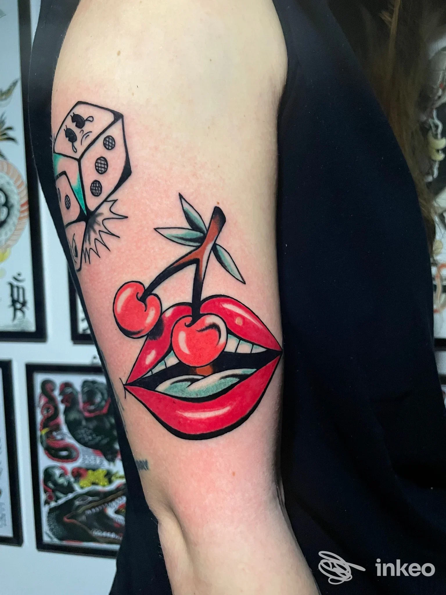 Tatuaggio sul braccio superiore raffigurante labbra con ciliegie e un dado in stile old school, fotografato nello studio Aloha Kai Tattoo Club a Siracusa.