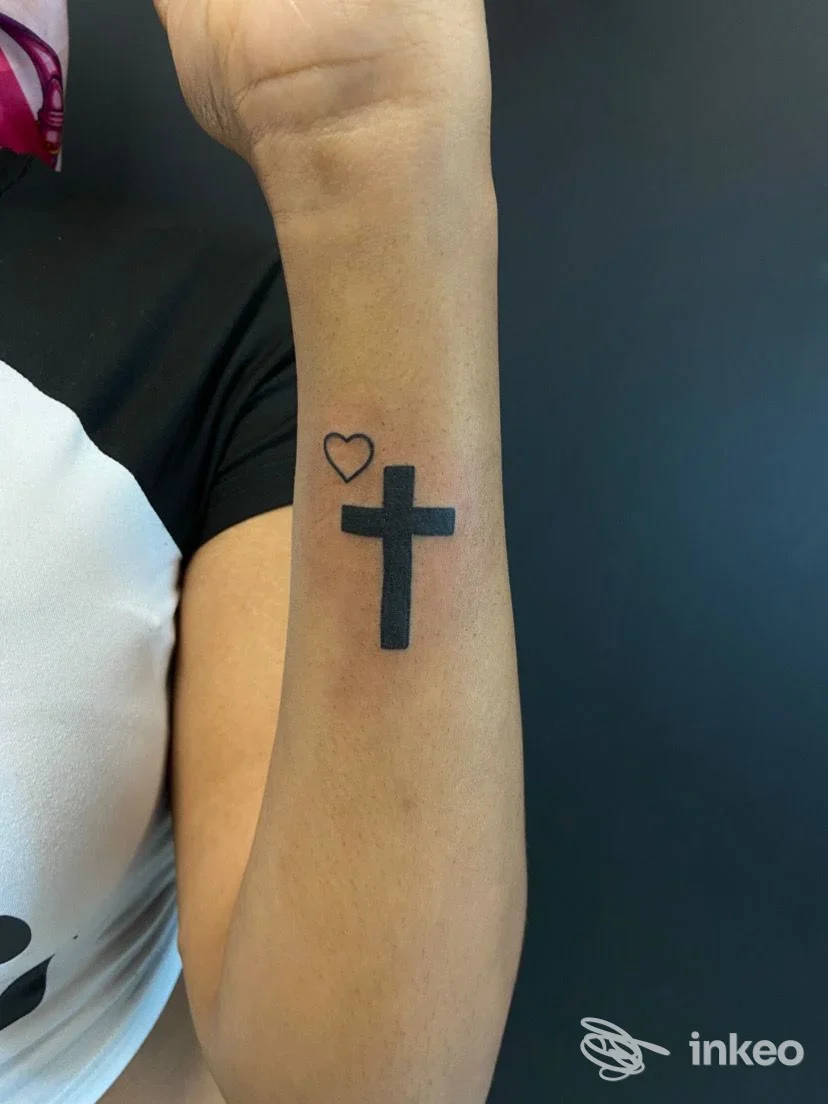 Tatuaggi sull'avambraccio interno: una croce piena nera e un piccolo cuore contornato. Immagine dallo studio American Dream Tattoos, Palermo.