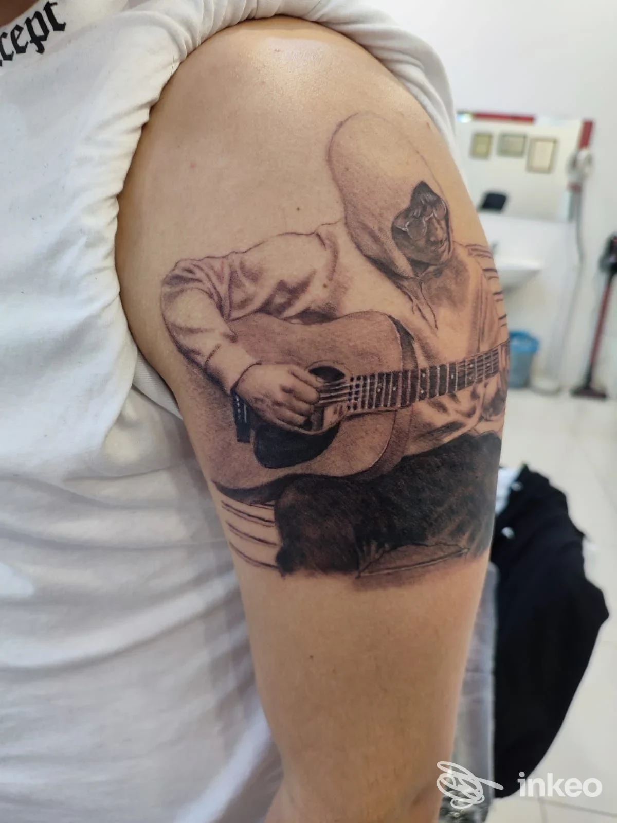 Tatuaggio realistico in bianco e nero sul braccio superiore raffigurante una figura con cappuccio che suona una chitarra — Amon Tattoo & Piercing, Ragusa