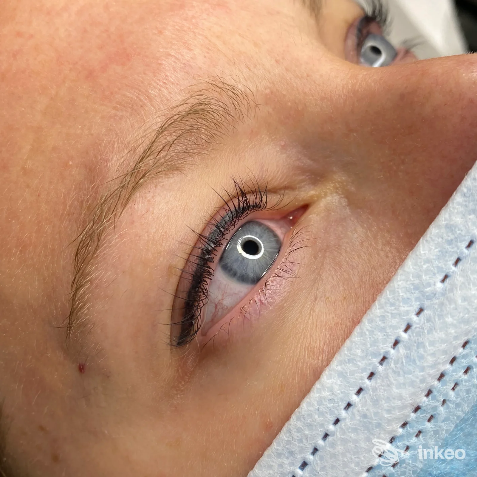 Primo piano dell'occhio di una persona con trucco permanente per eyeliner applicato sulla palpebra superiore, la palpebra è visibile insieme all'occhio azzurro.