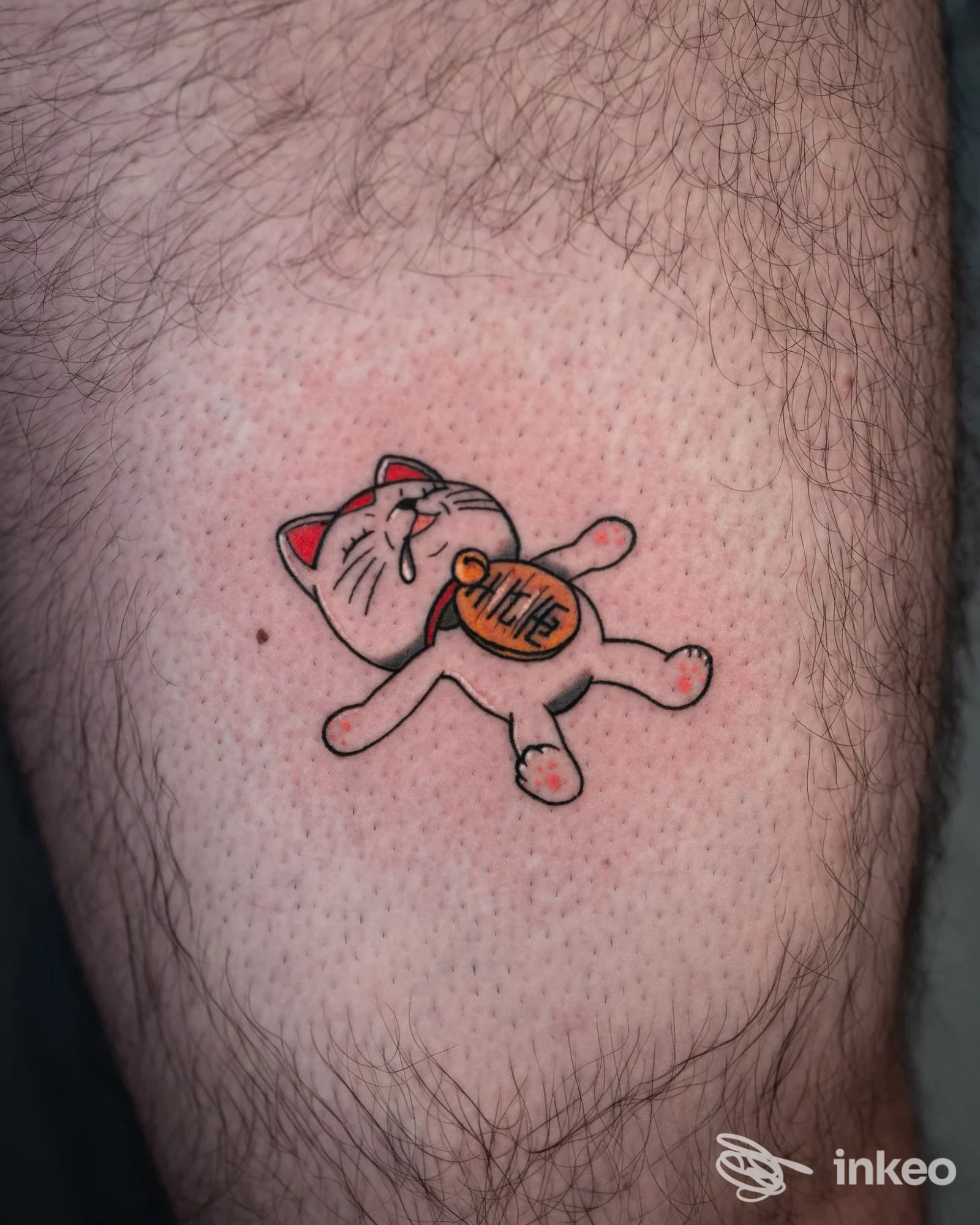 Tatuaggio su coscia di piccolo gatto portafortuna, lavoro mostrato da Bānum Tattoo Studio, Palermo.