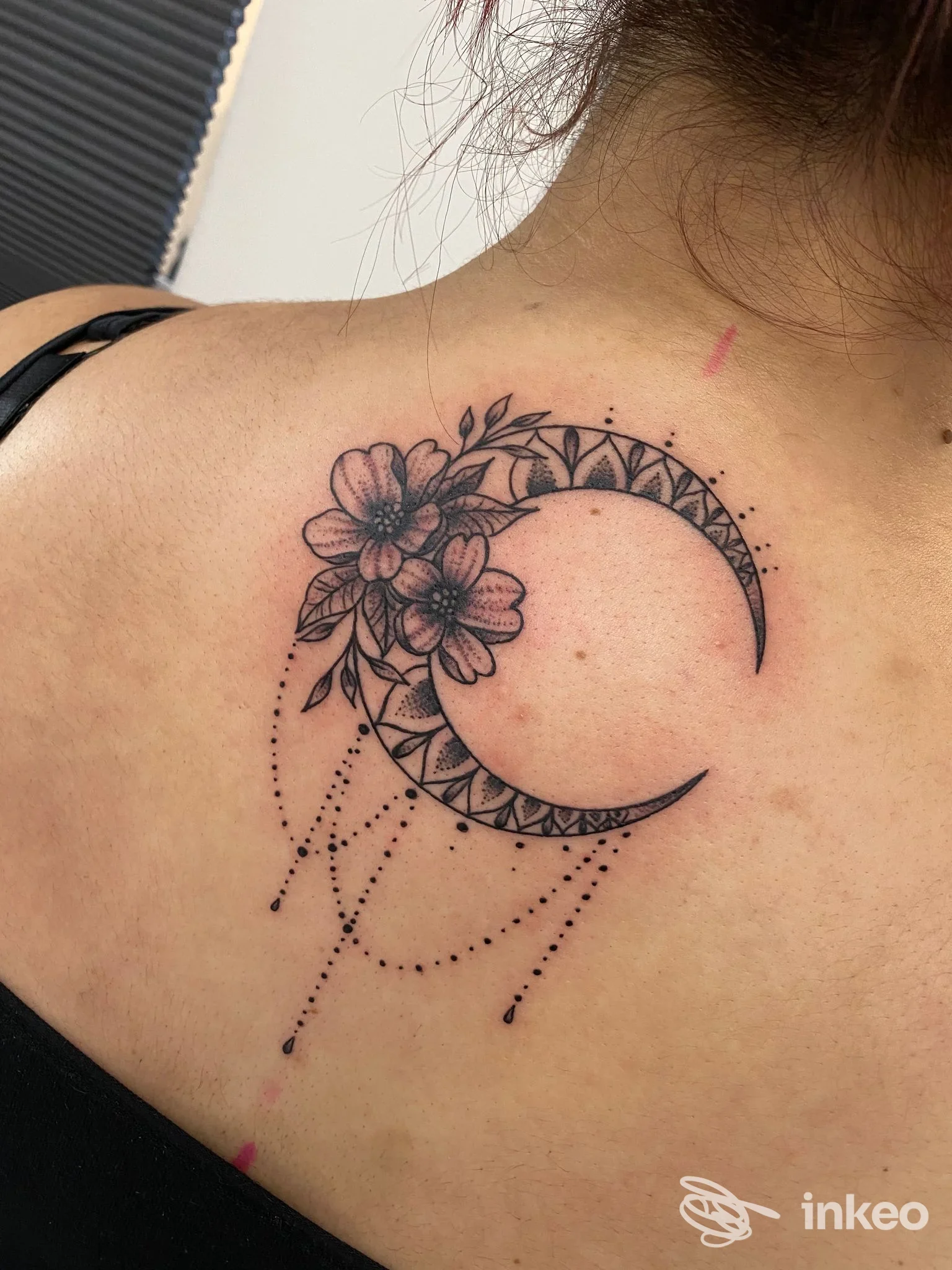 Tatuaggio a mezzaluna con fiori e pendenti sulla parte superiore della schiena, scatto del Black Soul Tattoo a Giardini-Naxos.