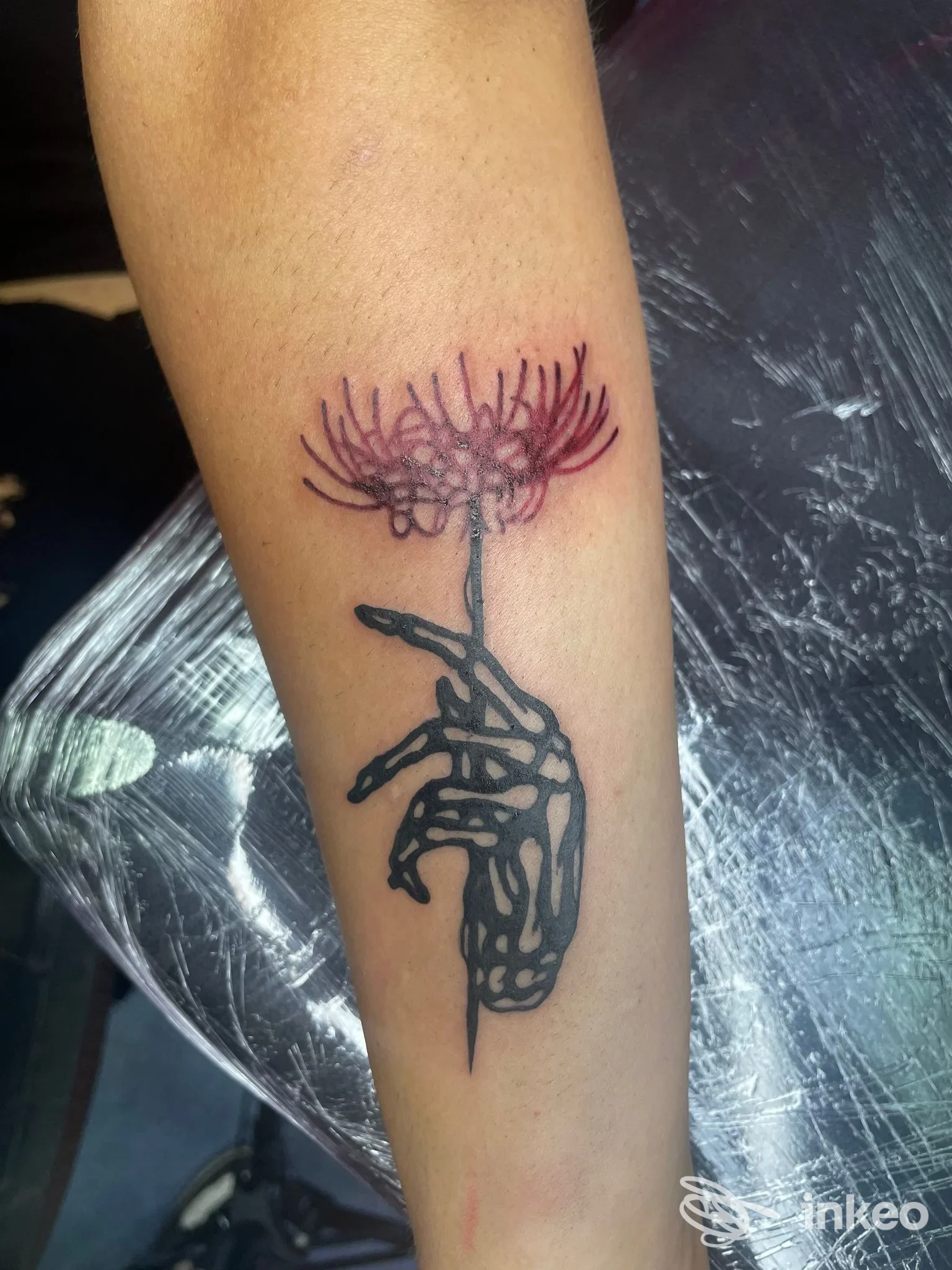 Tatuaggio su avambraccio: mano scheletrica che regge un fiore con petali rossastri, Catania Tattoo Studio, Catania.