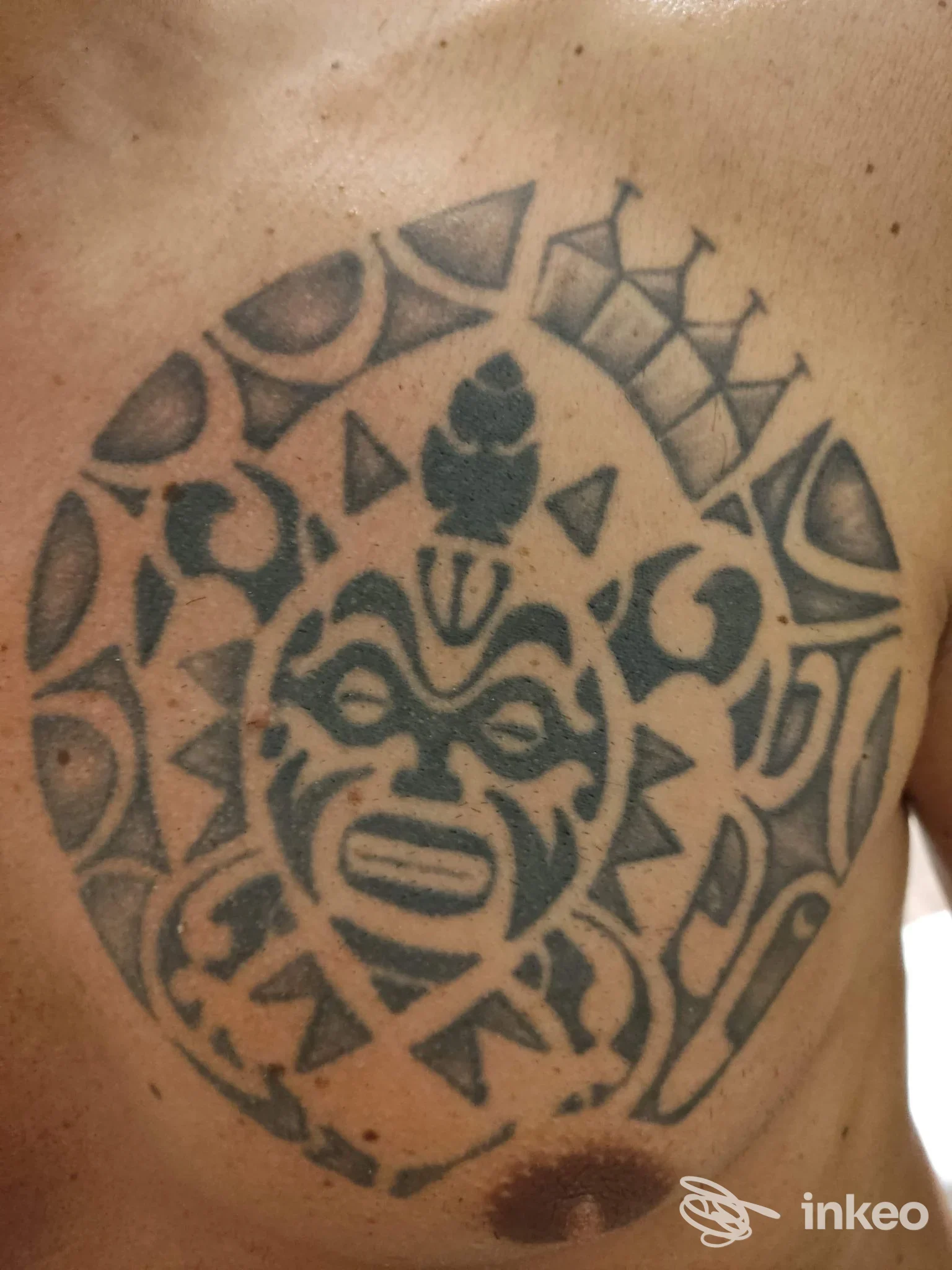 Tatuaggio circolare tribale sul petto con volto stilizzato al centro, realizzato su pelle. Cheeta Tattoo, Saponara Marittima.