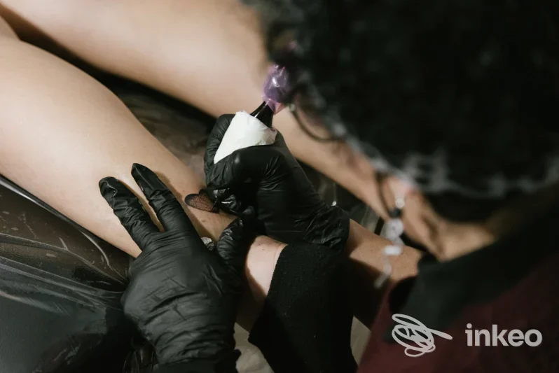Artista del Casamatta Tattoo Club di Favara mentre esegue un tatuaggio sul polpaccio di un cliente, dettaglio ravvicinato dell'intervento.