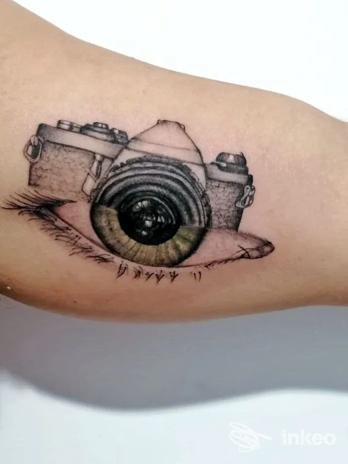 Tatuaggio su interno braccio raffigurante una macchina fotografica con obiettivo a forma d'occhio. Casamatta Tattoo Club, Favara.
